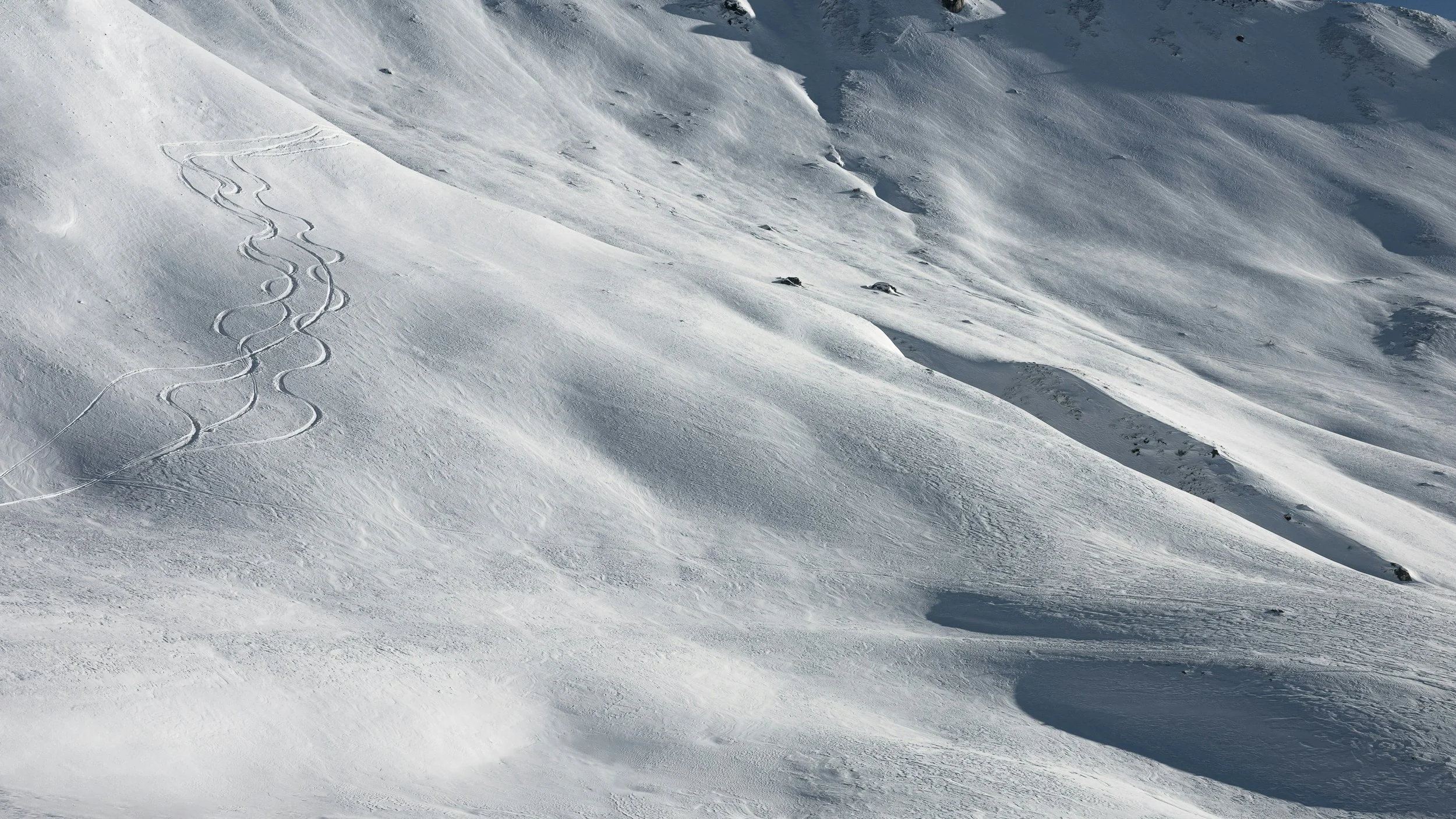 Snow-covered mountain slope with ski tracks and rocks.