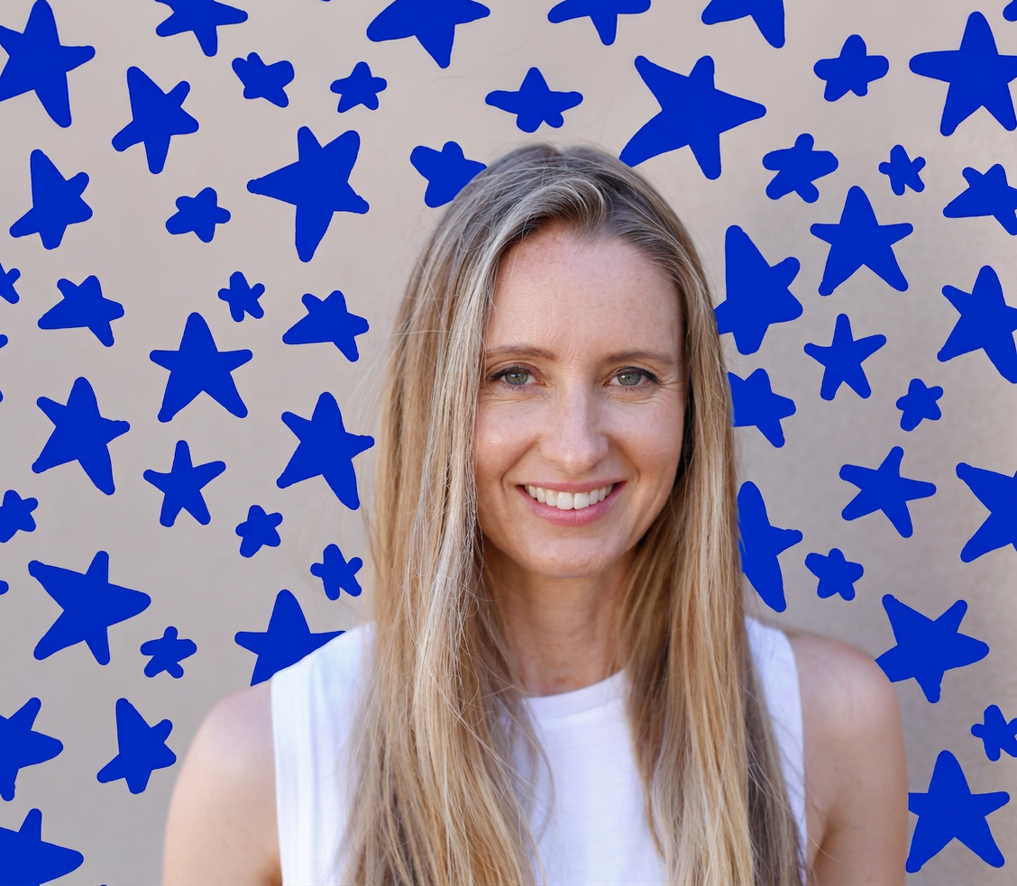 A woman with long blonde hair smiling in front of a wall decorated with blue star-shaped cutouts.