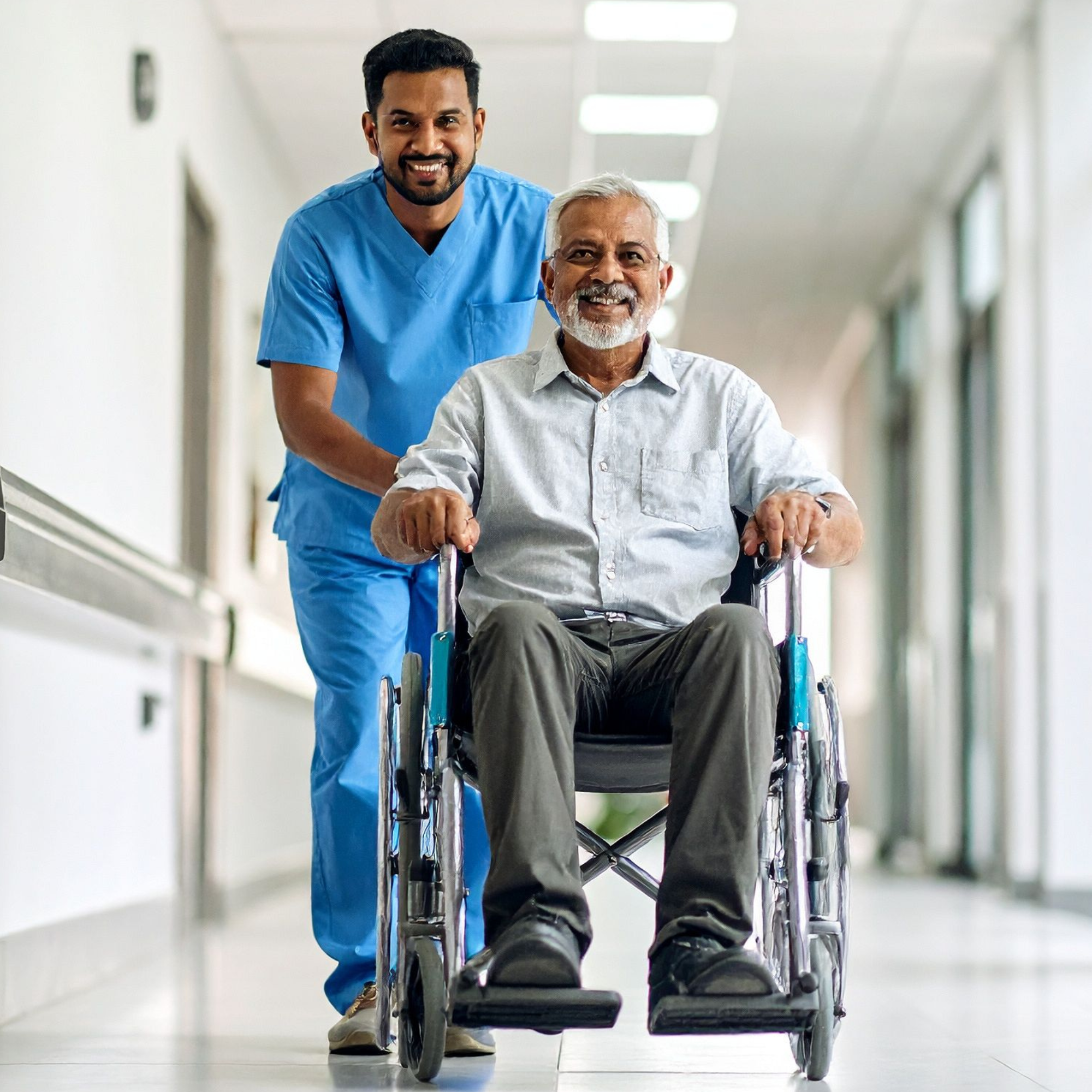 Healthcare professional pushing an elderly man in a wheelchair down a hospital corridor.