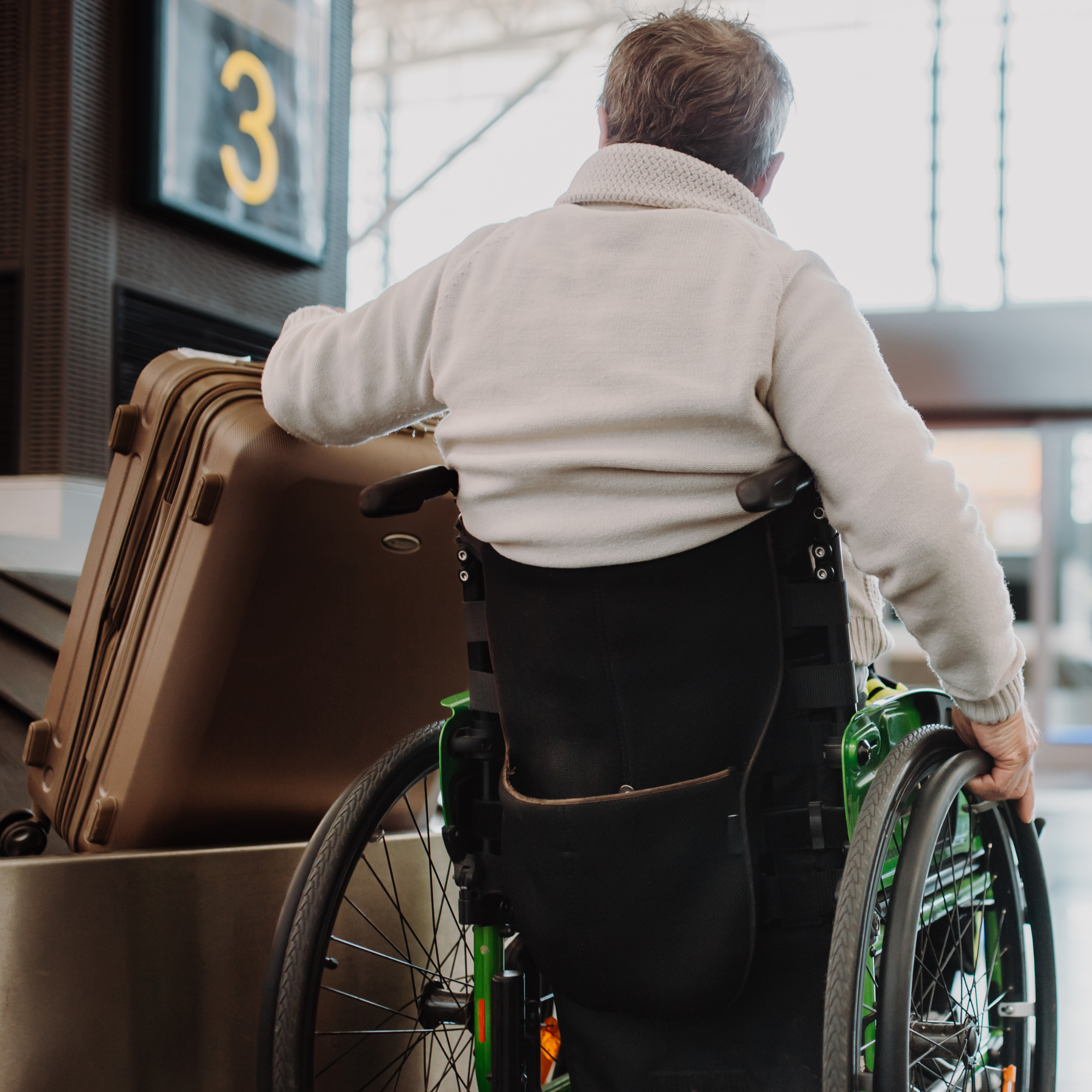 A person in a wheelchair waiting near an airport gate, with a sign displaying the letter 'C3' visible in the background.