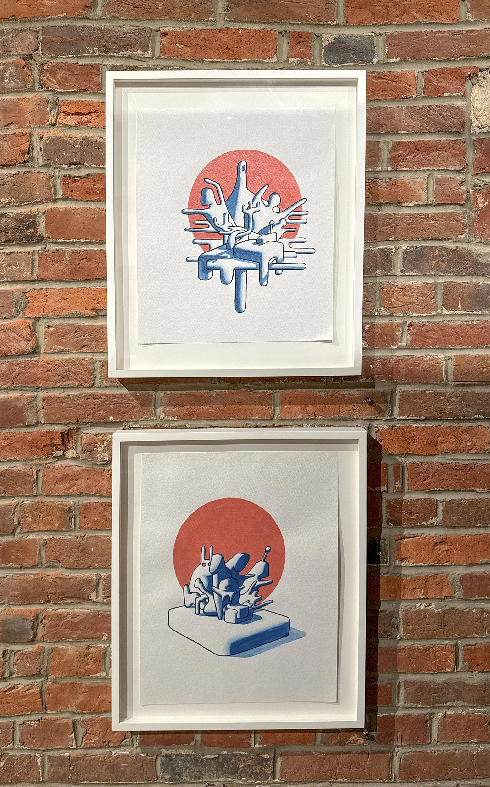 Two framed artworks on a brick wall, featuring abstract illustrations of blue animal-like figures with a red circular background.