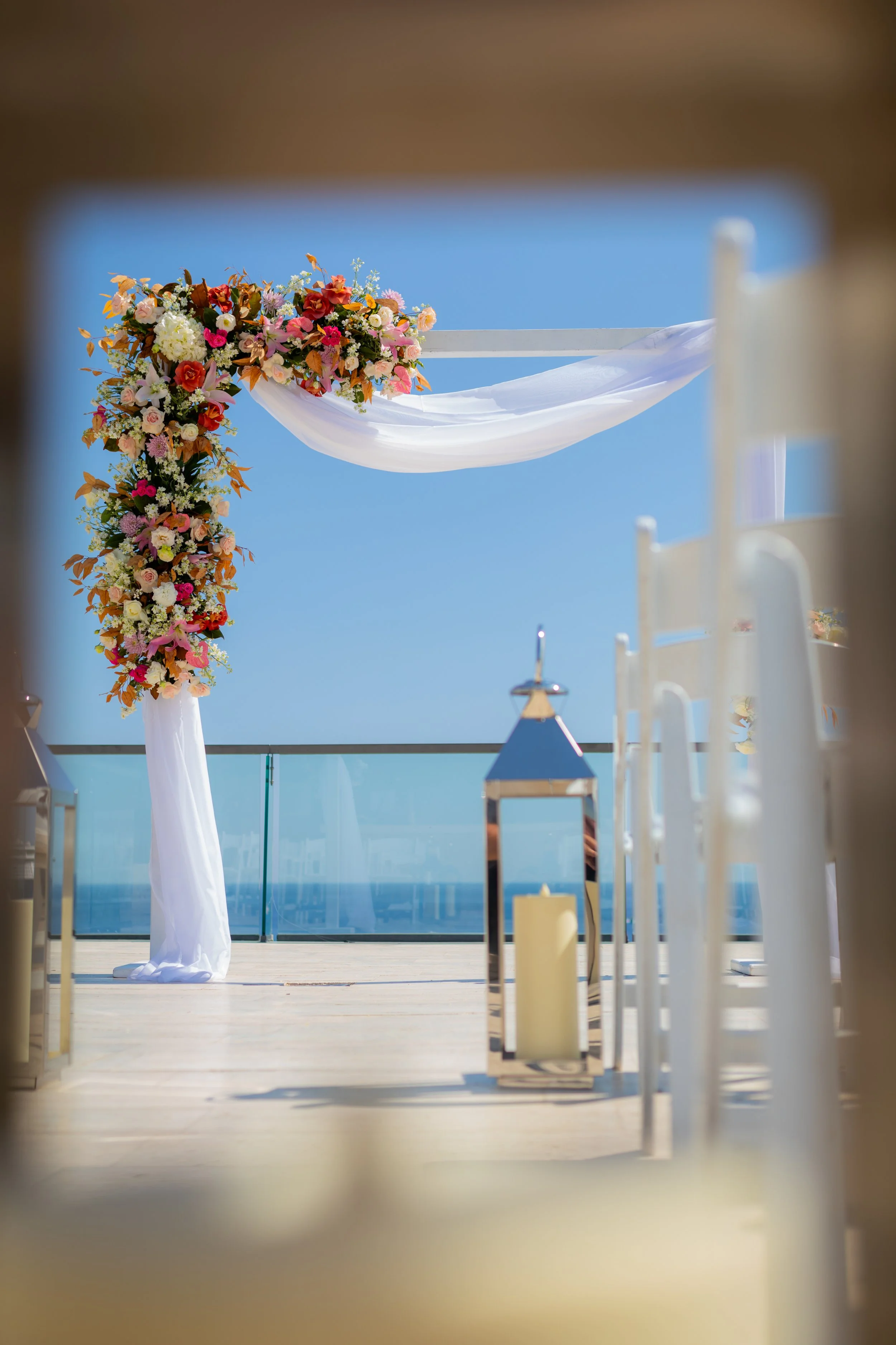 Los Cabos wedding ceremony arch with colorful florals, white draping, ocean views, and ceremony decor by I DO Weddings Los Cabos.