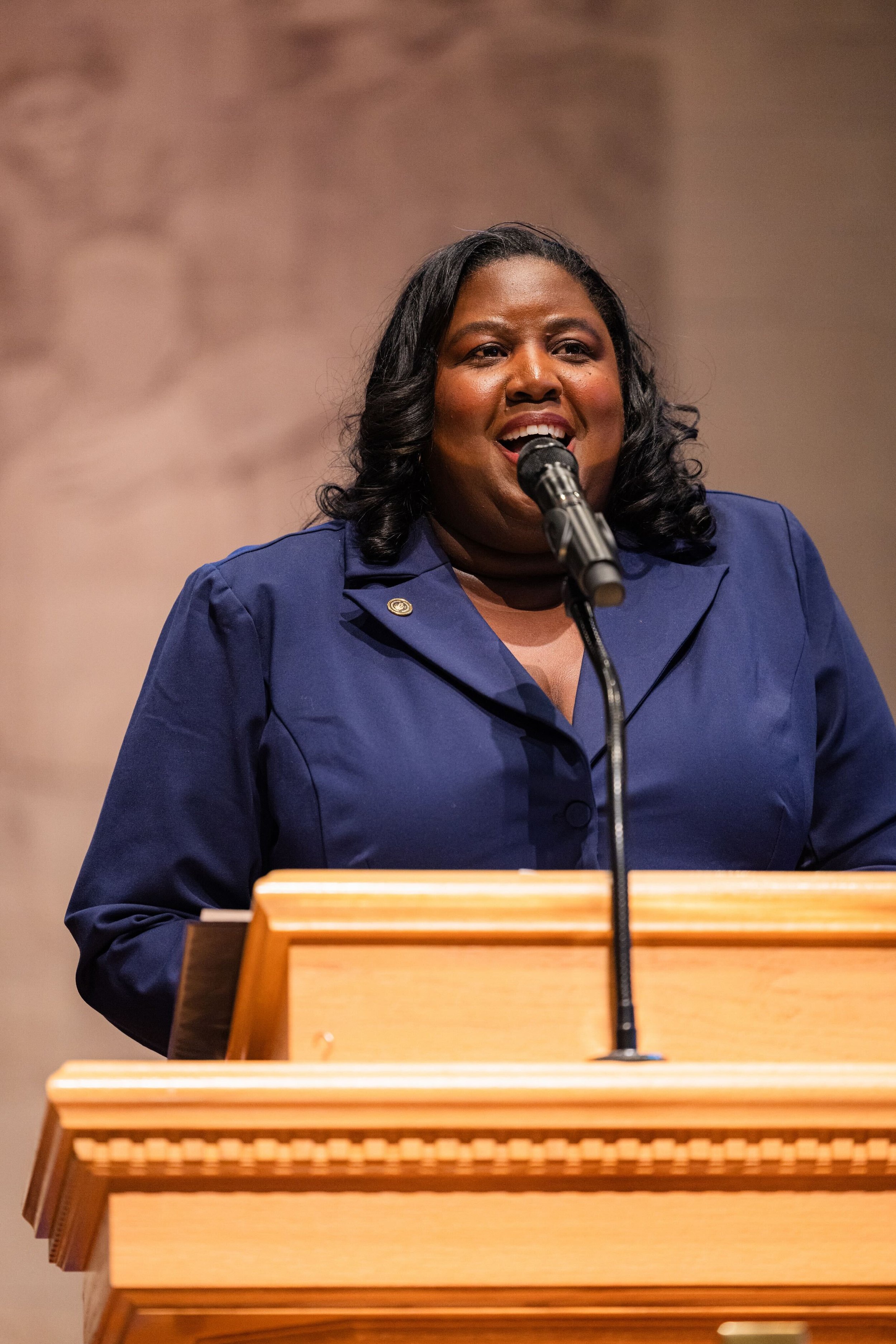 Monchiere' Holmes Jones, Cultural Economist™  with speaking at a podium, wearing a blue blazer, at American Baptist College.