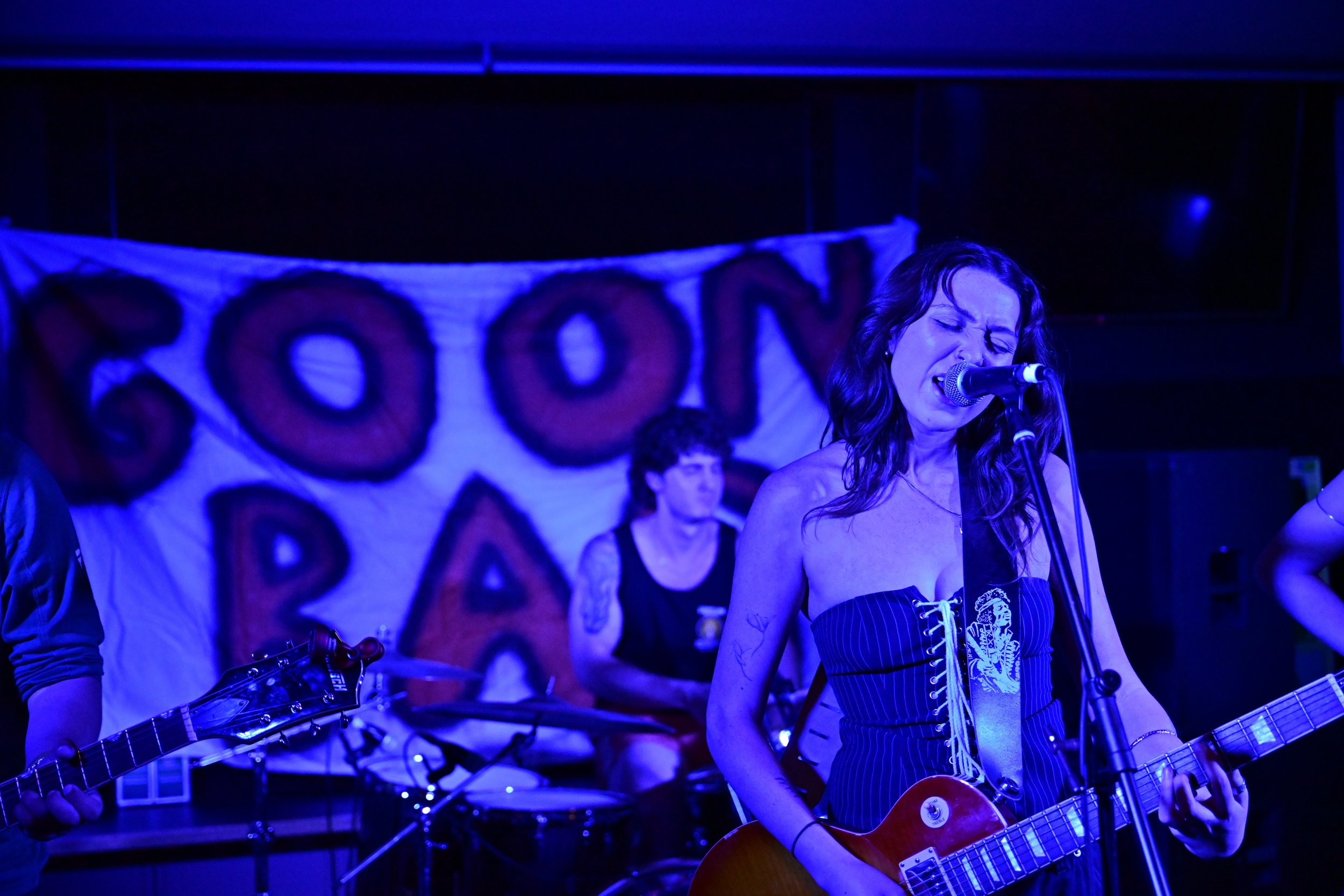 A woman singing into a microphone and playing an electric guitar on stage, with a banner in the background that reads 'POIN'.