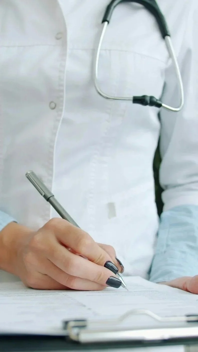 Un medico che scrive su un documento con una penna, con uno stetoscopio appoggiato al camice.