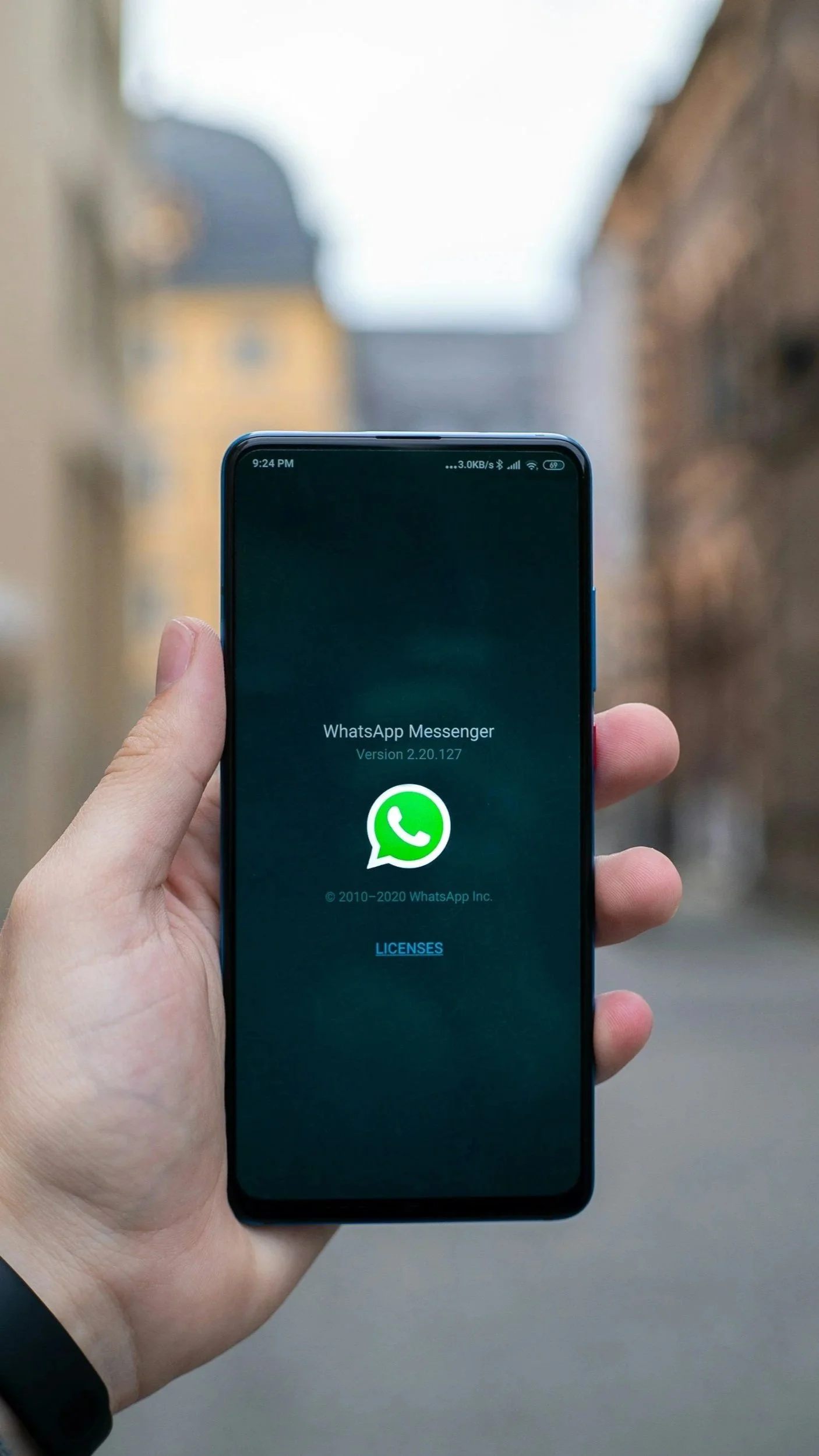 Persona che tiene in mano uno smartphone che mostra lo schermo di WhatsApp Messenger con la schermata di benvenuto.