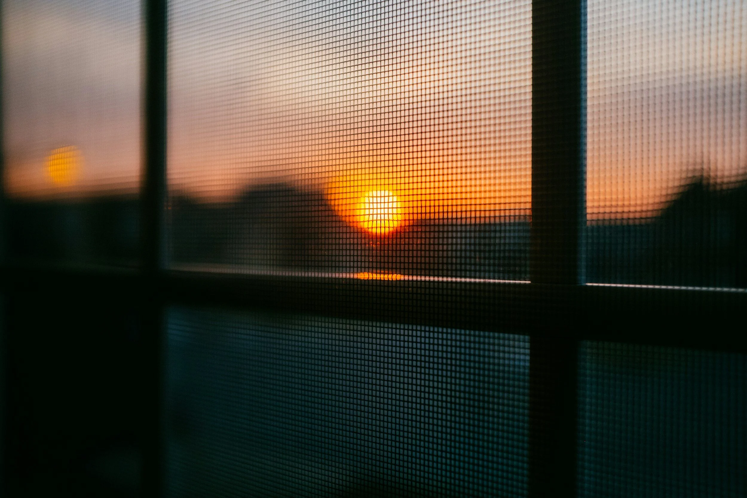 A sunset viewed through a window screen with vertical bars.