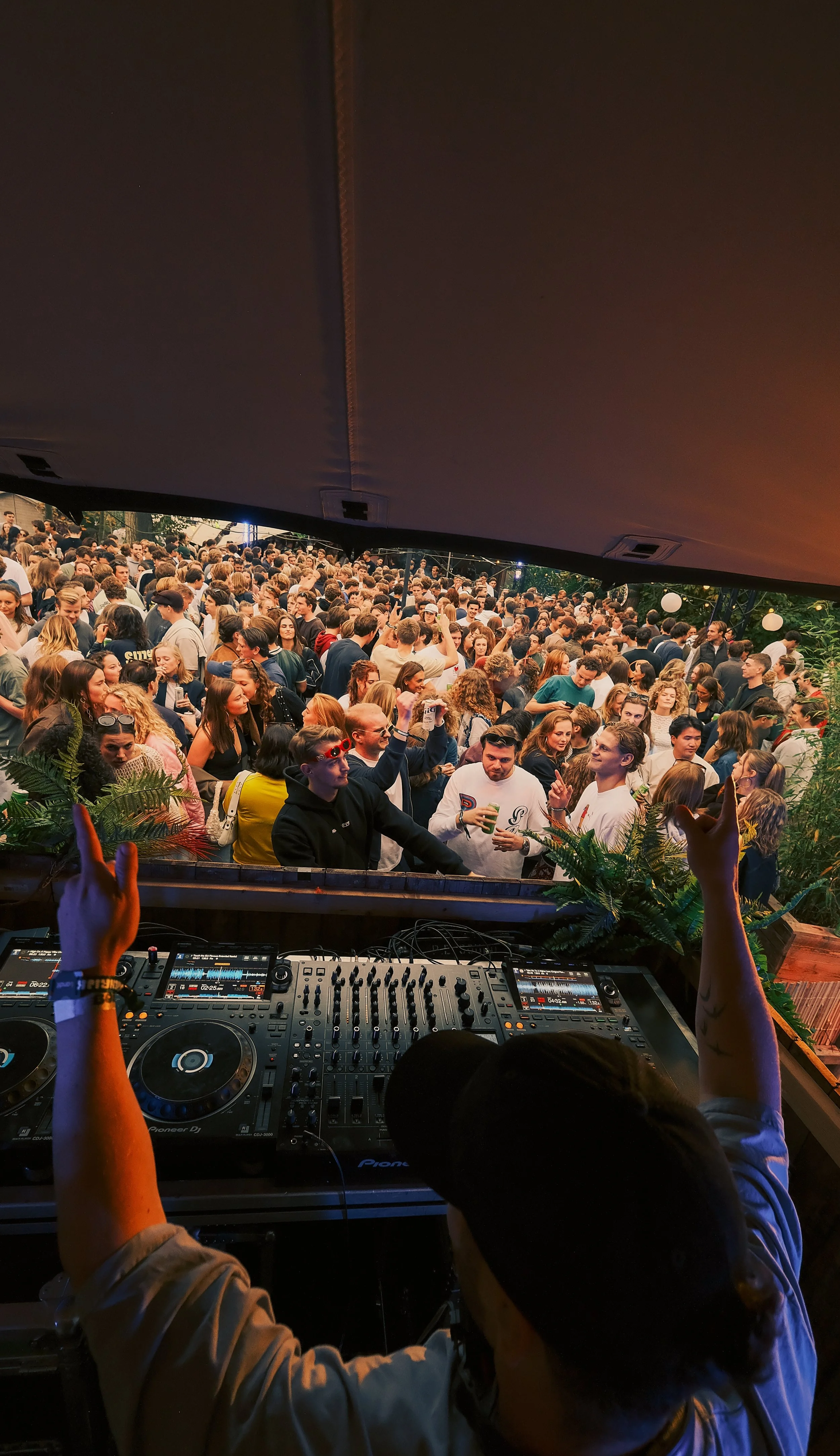 DJ draait muziek voor grote menigte op openluchtfeest, mensen dansen en beleven plezier.