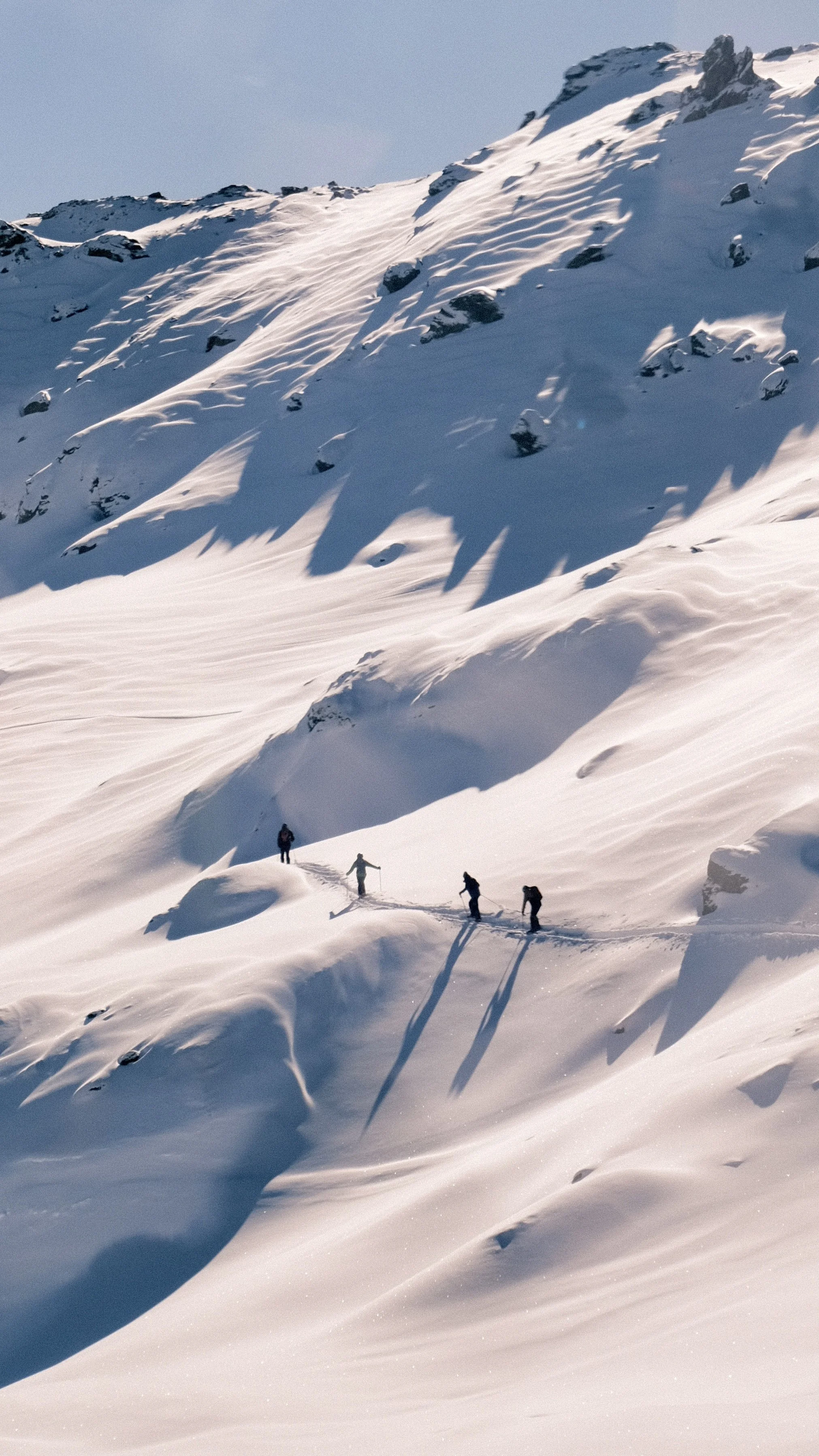 Vier mensen maken een sneeuwwandeling op een besneeuwd berglandschap met rotsen en een blauwe lucht.