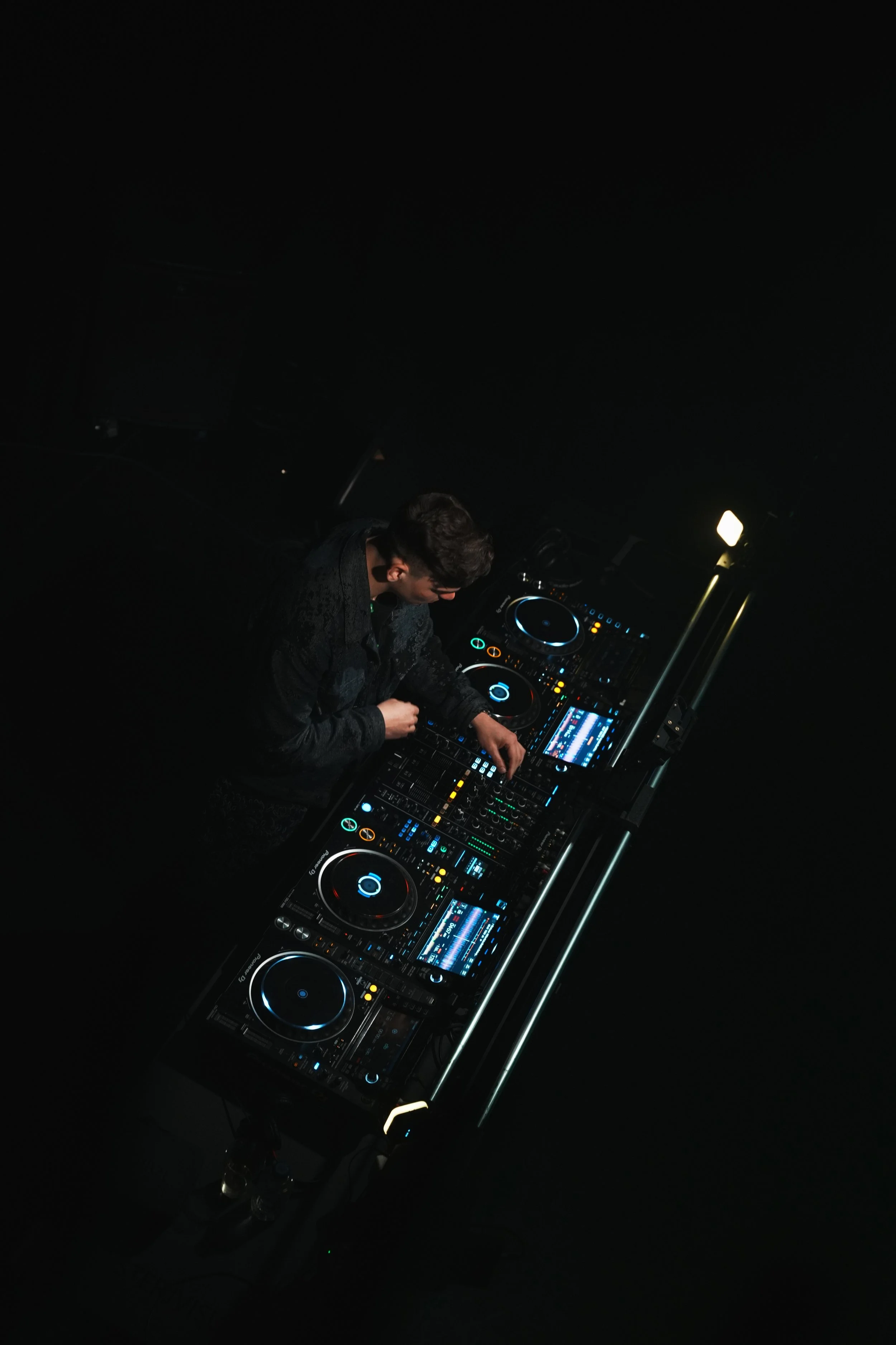 een dj die muziek draait achter een DJ mixer met verlichting, in een donkere kamer of club