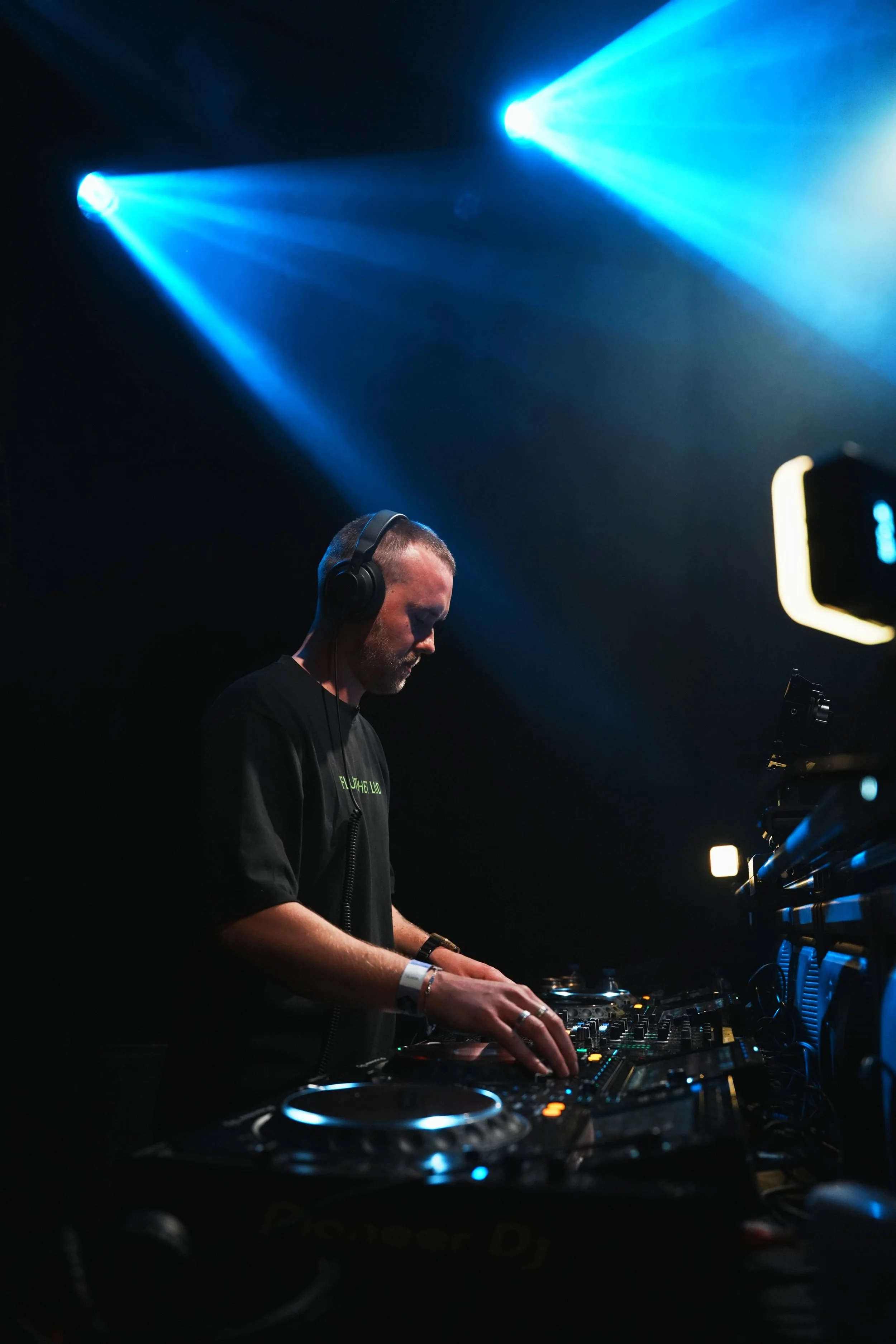 Een man achter een DJ-mixer in een donkere omgeving, verlicht door blauwe lichten.