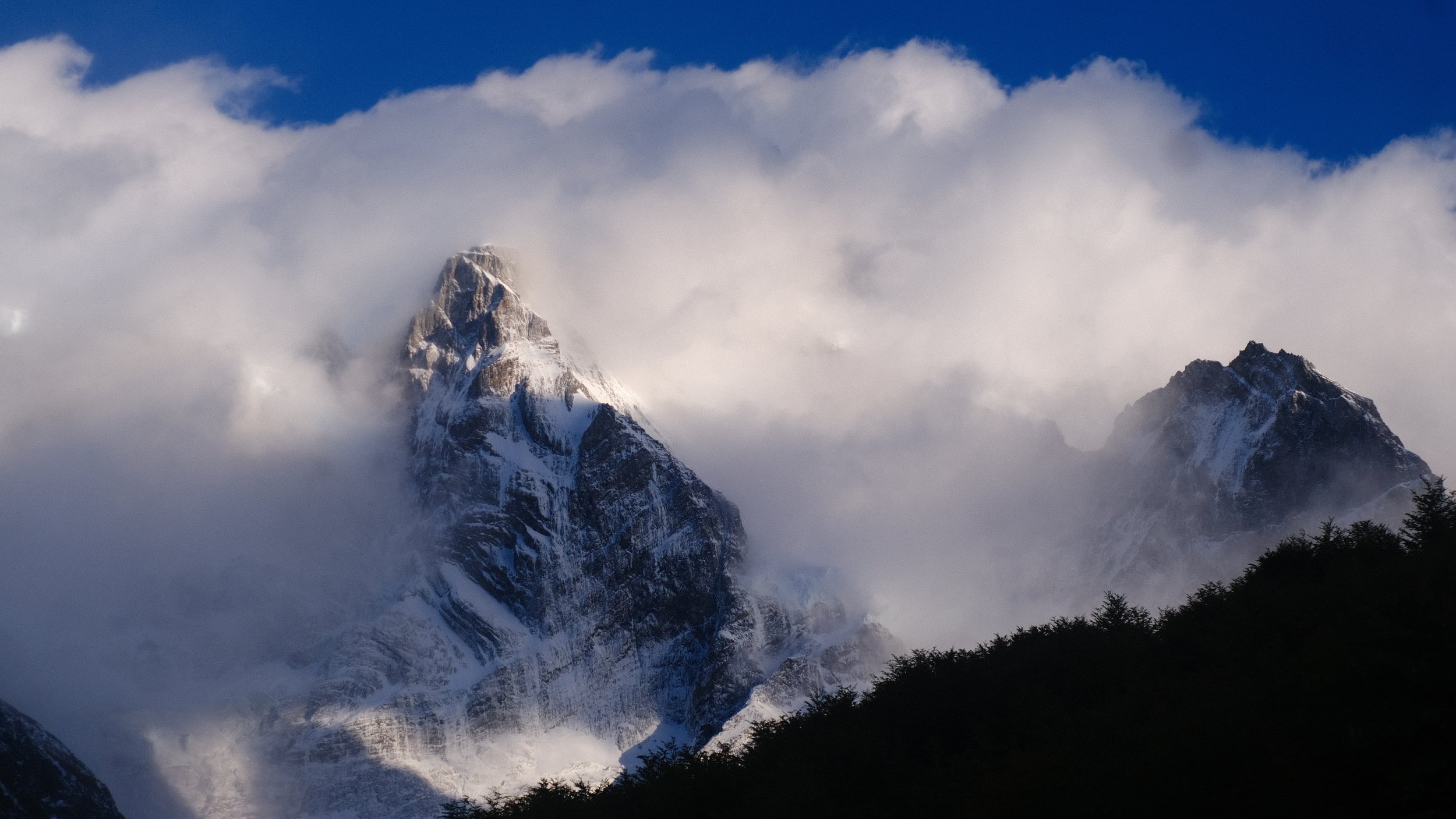 Sneeuwbedekte bergtoppen met wolken en een blauwe lucht.