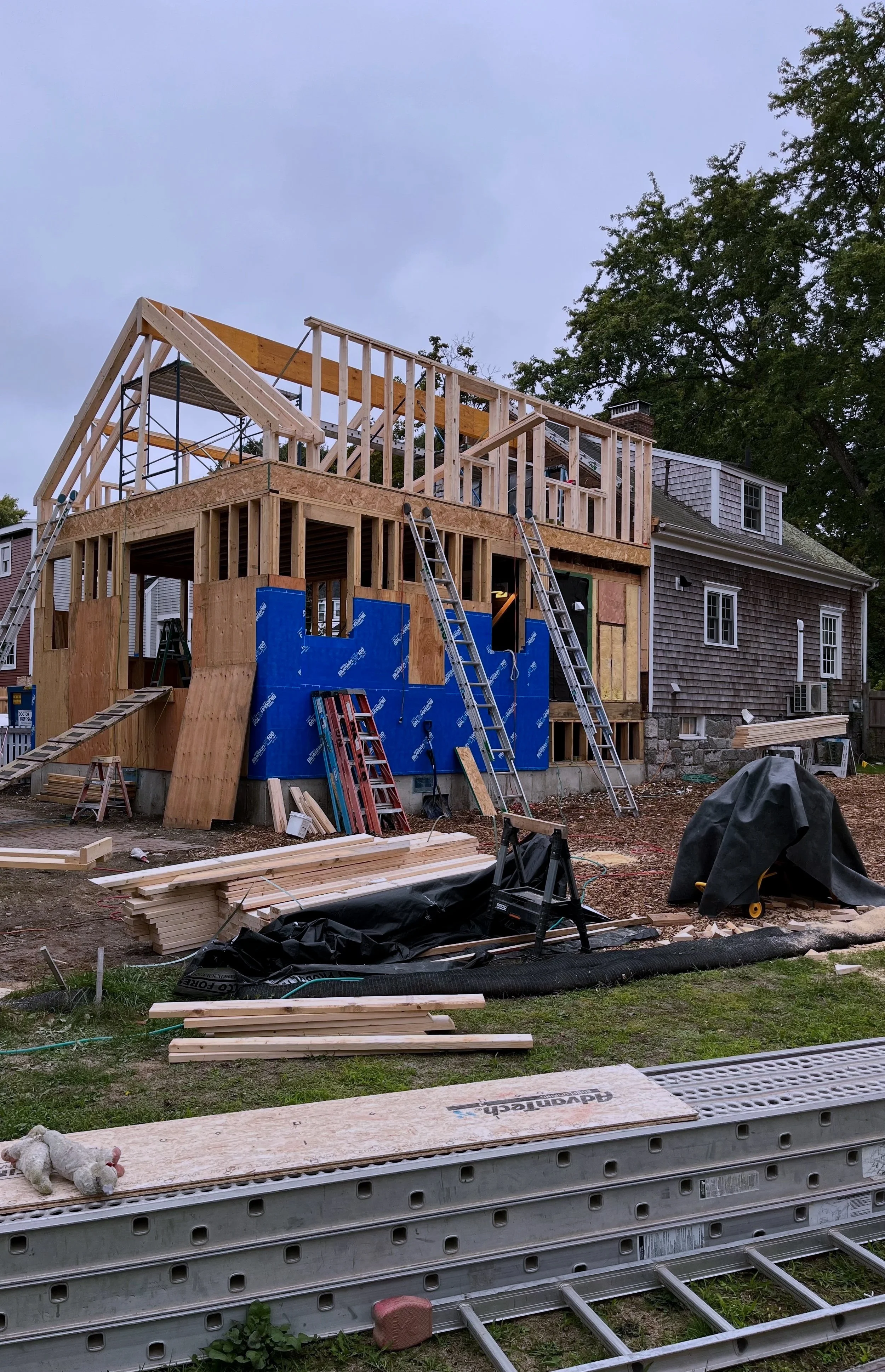 Construction site with the framework of a house being built, ladders, building materials, and tools scattered around.