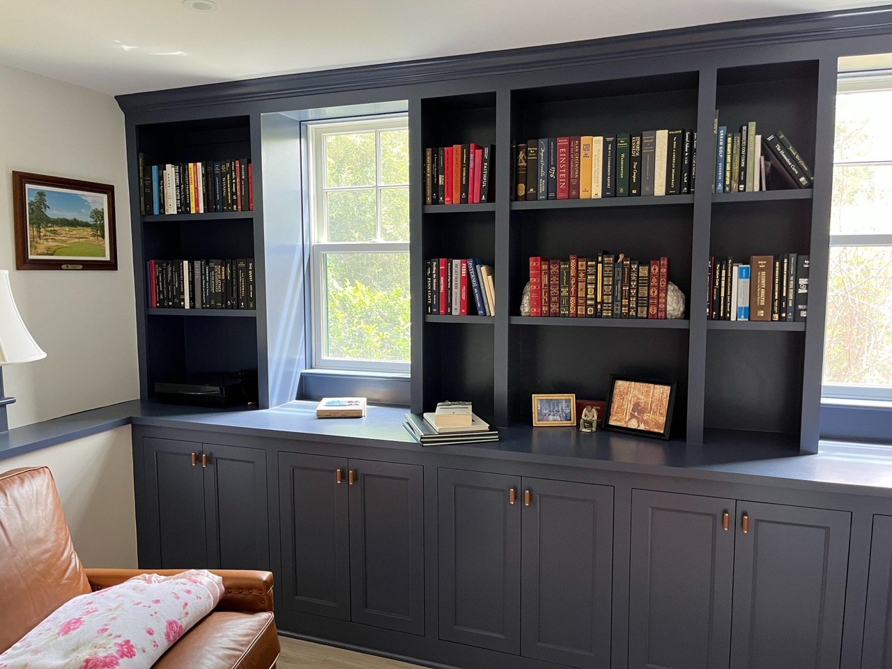 Blue built-in bookshelf with books, framed photographs, and decorative items, near a window in a living room.