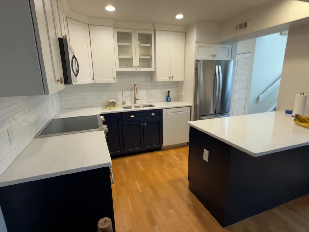 Modern kitchen with white upper cabinets, dark lower cabinets, stainless steel refrigerator, white countertops, and a white subway tile backsplash.