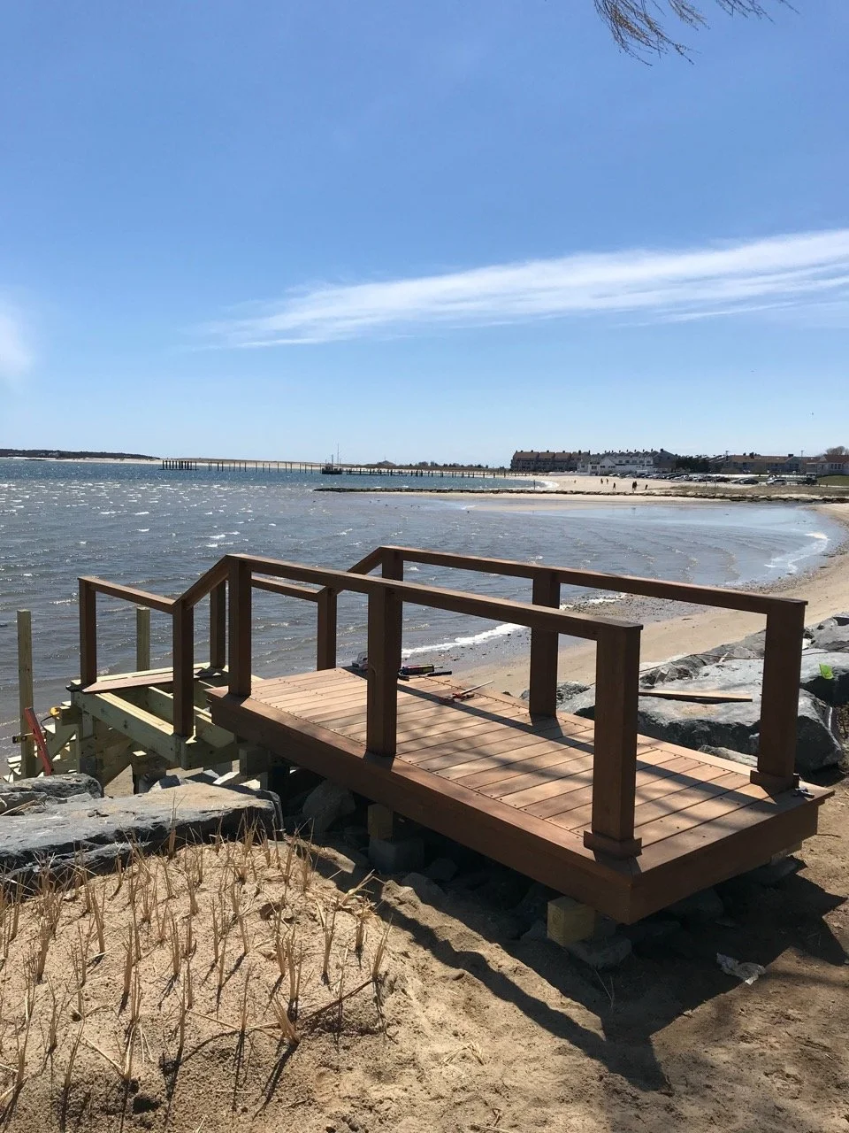 A wooden platform with safety railings built over rocks and sand along a beach, with the ocean and sky in the background.