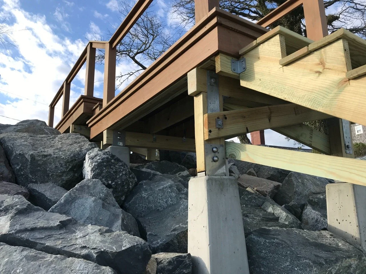 Wooden deck construction supported by metal and concrete supports on large rocks.