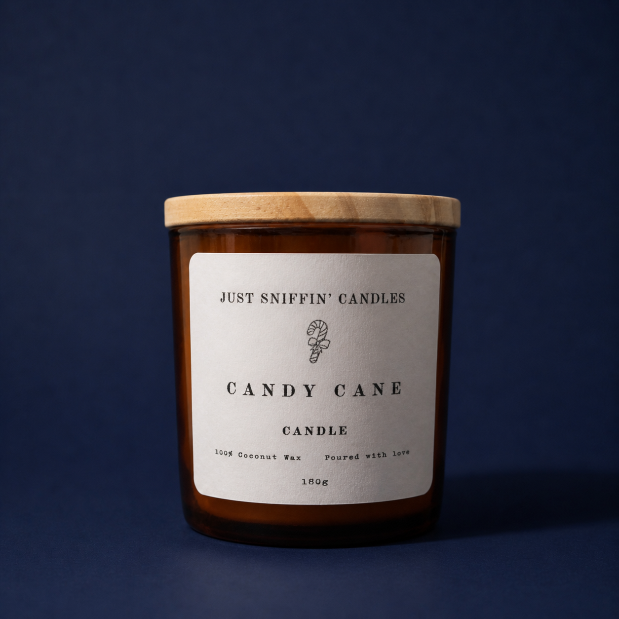 A brown candle jar with a wooden lid labeled 'Just Sniffin' Candles Candy Cane Candle,' featuring a small candy cane illustration, set against a dark blue background.