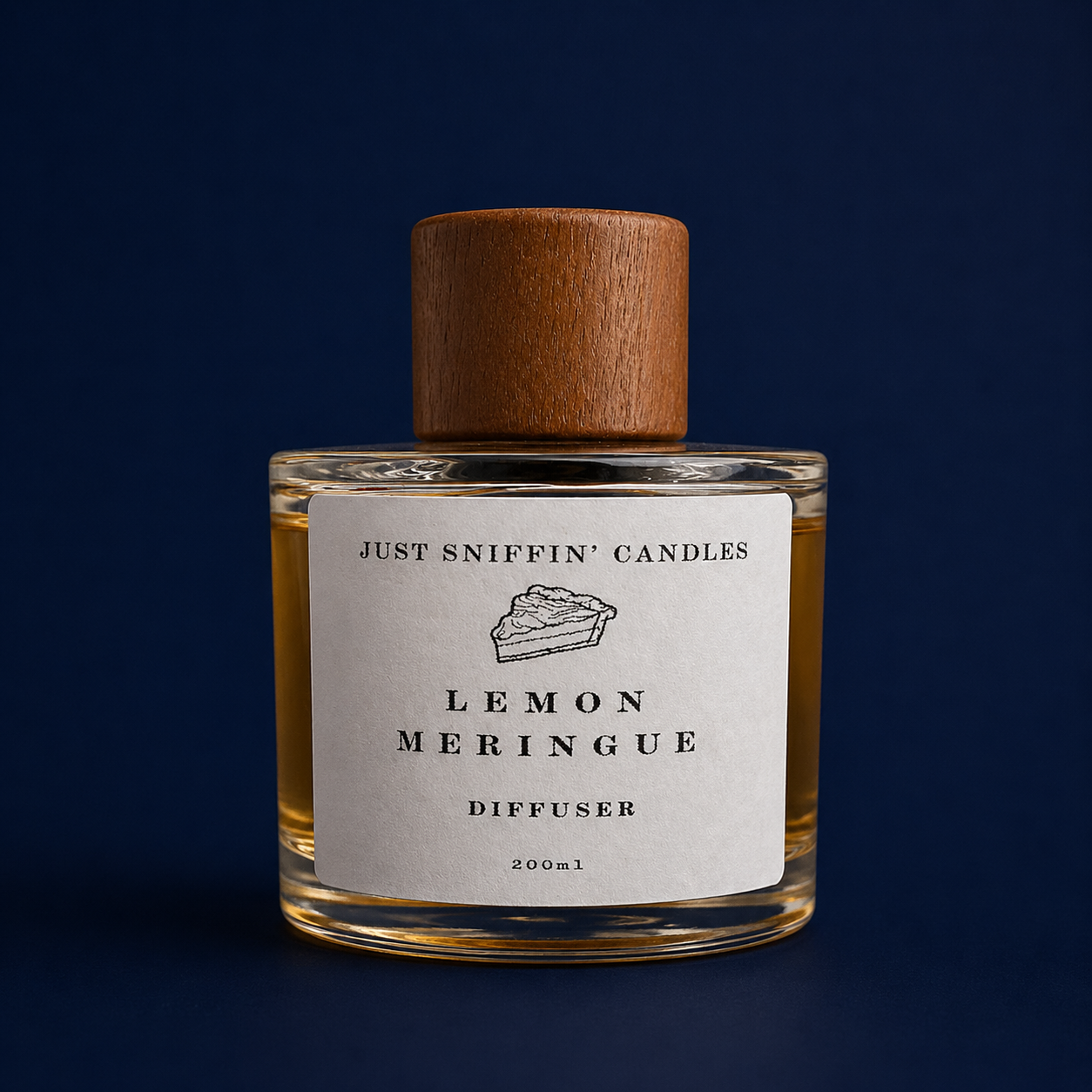A glass diffuser bottle labeled 'Lemon Meringue,' with a wooden cap, photographed against a dark blue background.