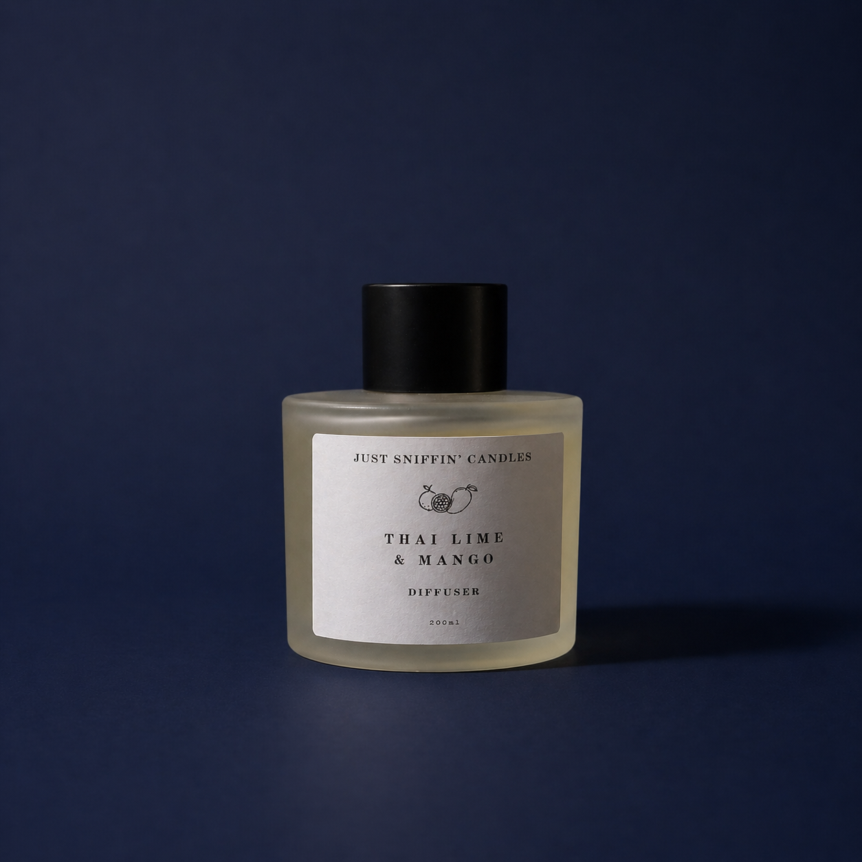 A frosted glass diffuser bottle with a black cap, labeled 'Just Sniffin' Candles, Thai Lime & Mango, Diffuser, 200ml,' placed against a dark blue background.