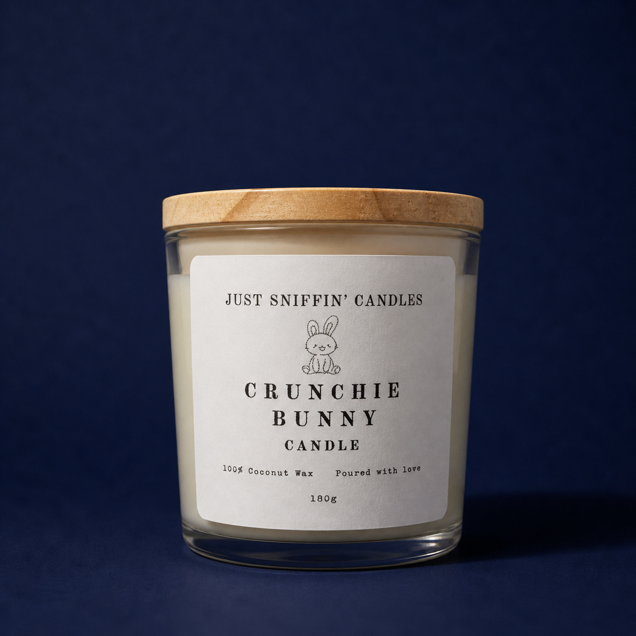 A candle in a glass jar with a wooden lid, labeled 'Crunchie Bunny Candle' with a cute bunny illustration, on a dark blue background.