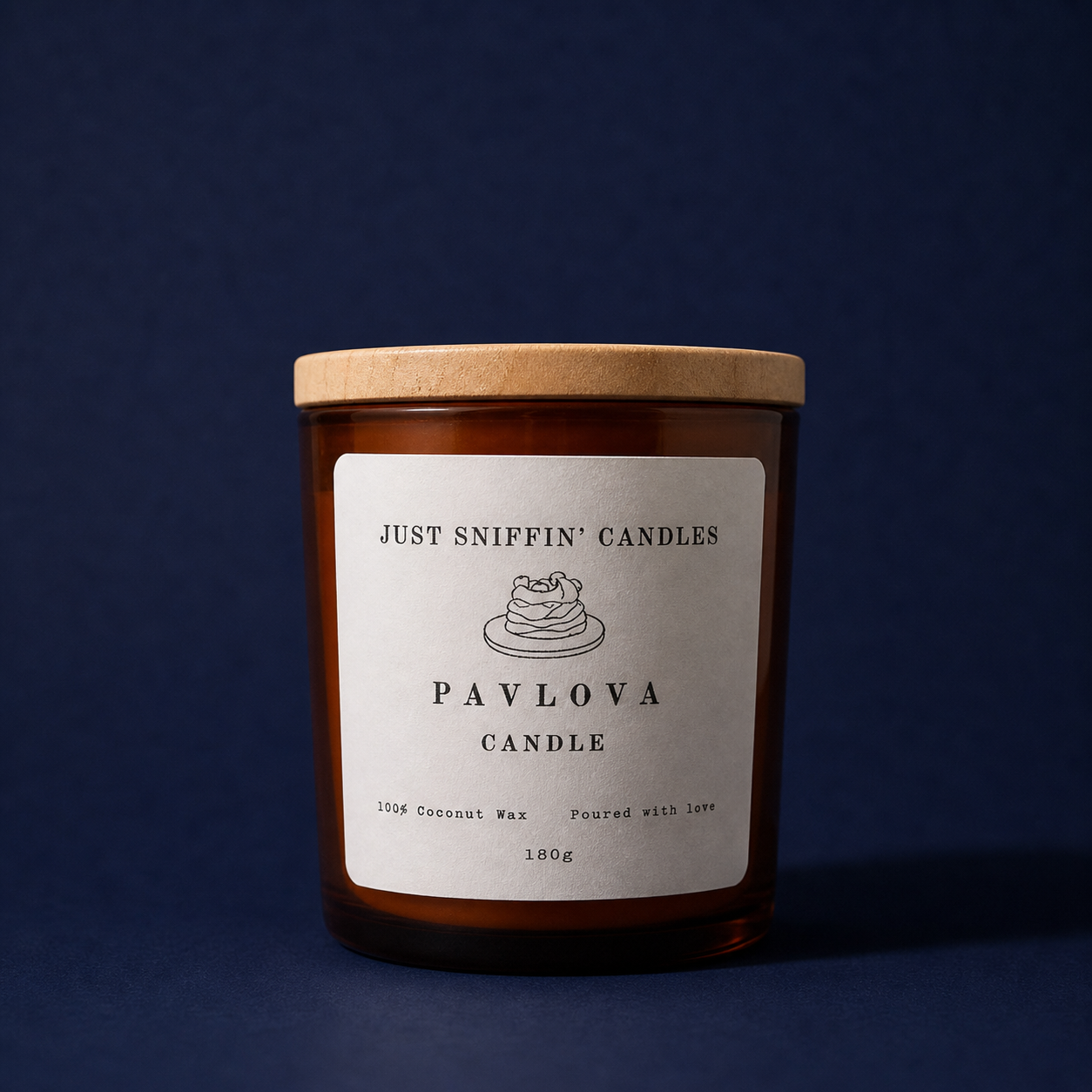 Brown candle jar with a wooden lid labeled 'Just Sniffin' Candles Pavlova Candle,' featuring a simple illustration of pavlova dessert, on a dark blue background.