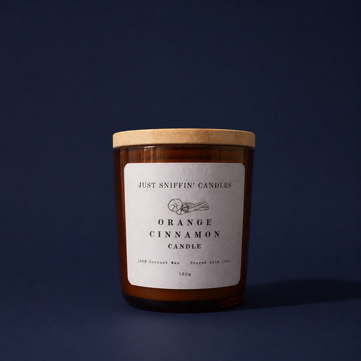 A brown candle jar with a wooden lid, labeled 'Just Sniffin' Candles Orange Cinnamon Candle,' with a simple white label, placed against a dark blue background.