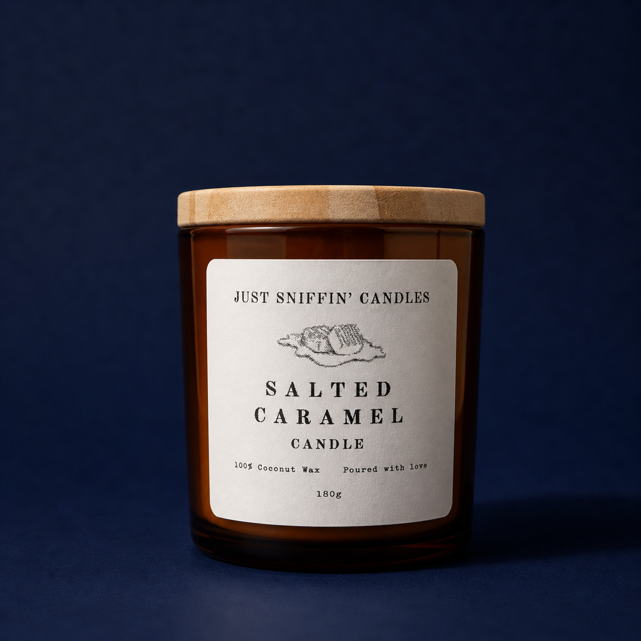 A brown glass candle jar with a wooden lid, labeled 'Just Sniffin' Candles Salted Caramel Candle. 100% Coconut Wax, Poured with Love, 180g,' against a dark blue background.