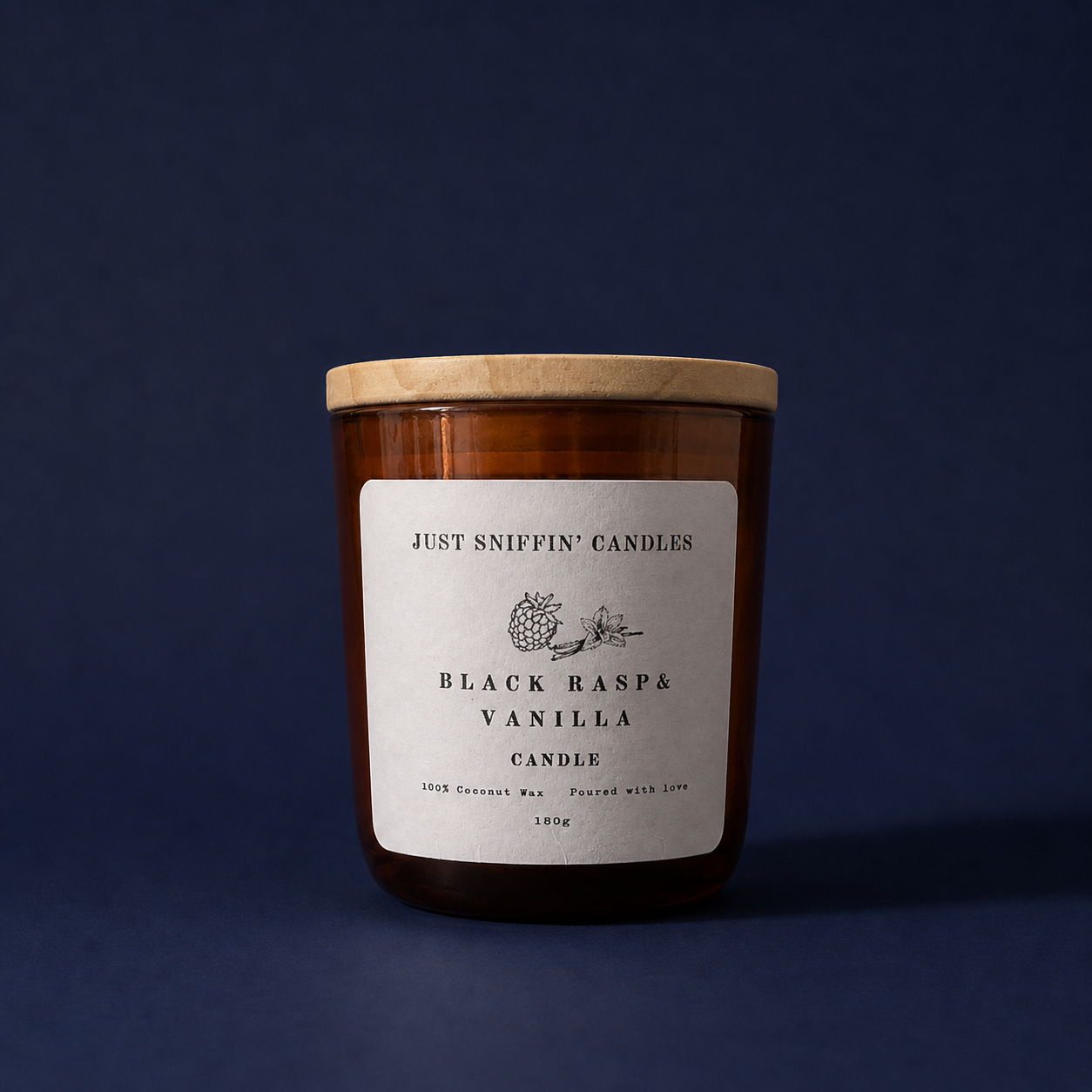 A brown candle jar with a light wood lid and a white label that reads "Just Sniffin' Candles" and "Black Rasp & Vanilla Candle". The label also indicates it is made from 100% coconut wax, 180 grams, and poured with love, set against a dark blue background.