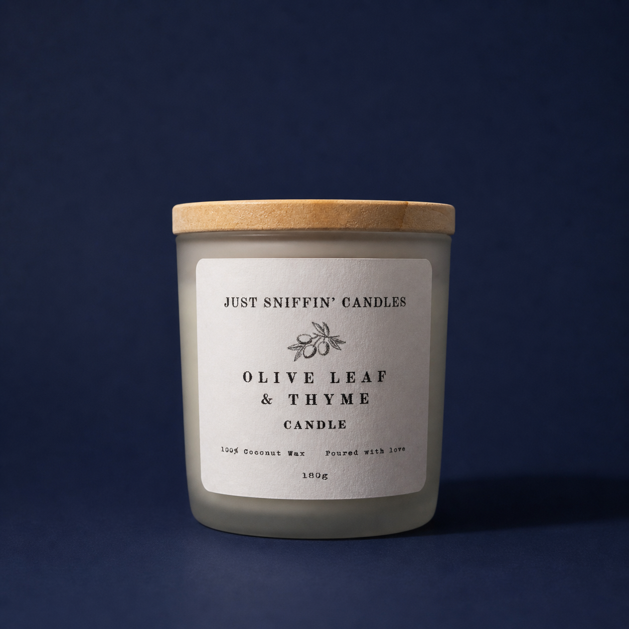 A white candle with a wooden lid labeled 'Just Sniffin' Candles Olive Leaf & Thyme Candle', made with coconut wax, weighing 180g, against a dark blue background.