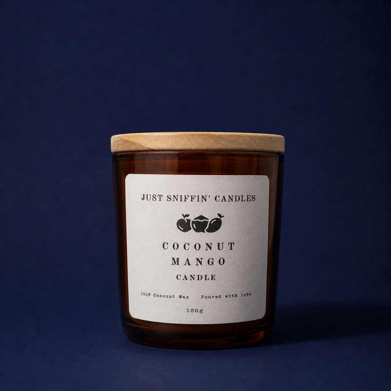 Amber glass jar candle with a wooden lid and white label reading 'Just Sniffin' Candles Coconut Mango Candle', set against a dark background.