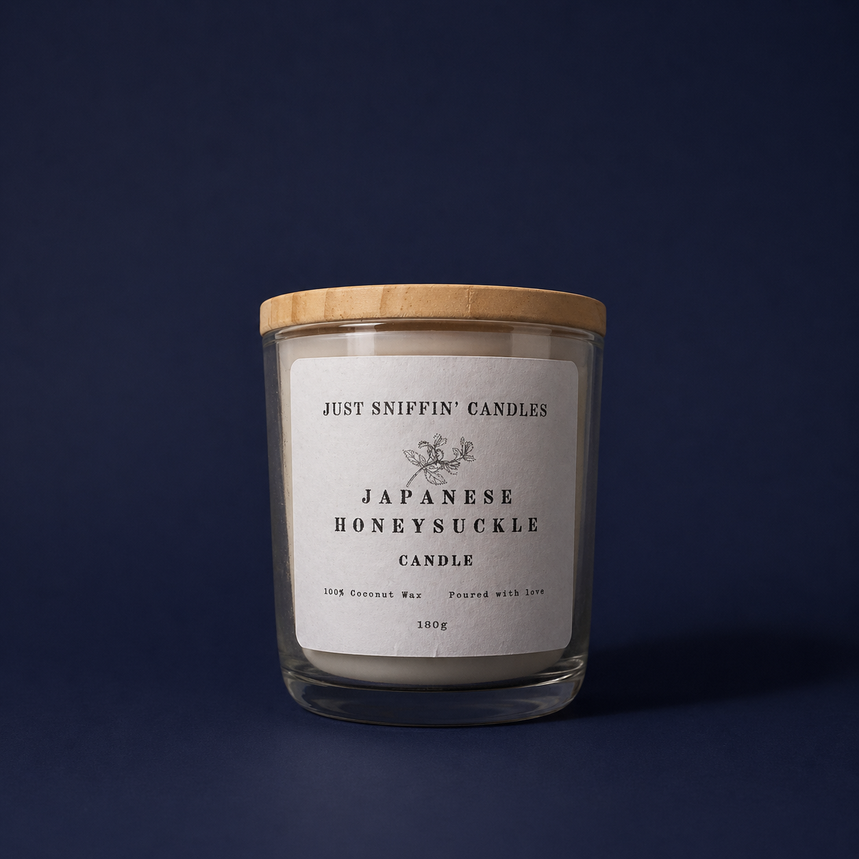 A candle in a glass jar with a wooden lid. The label reads 'Just Sniffin' Candles, Japanese Honeysuckle Candle, 100% Coconut Wax, Poured with Love, 180g'.