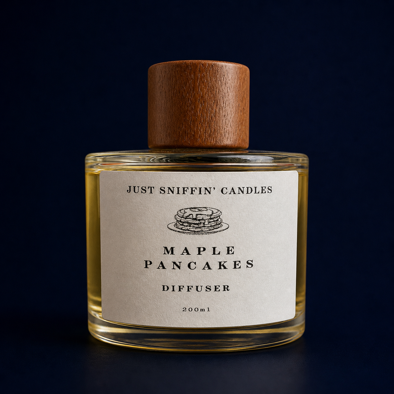 A glass candle jar with a wooden lid, labeled 'Just Sniffin' Candles Maple Pancakes Diffuser' with a small pancake illustration, set against a dark background.