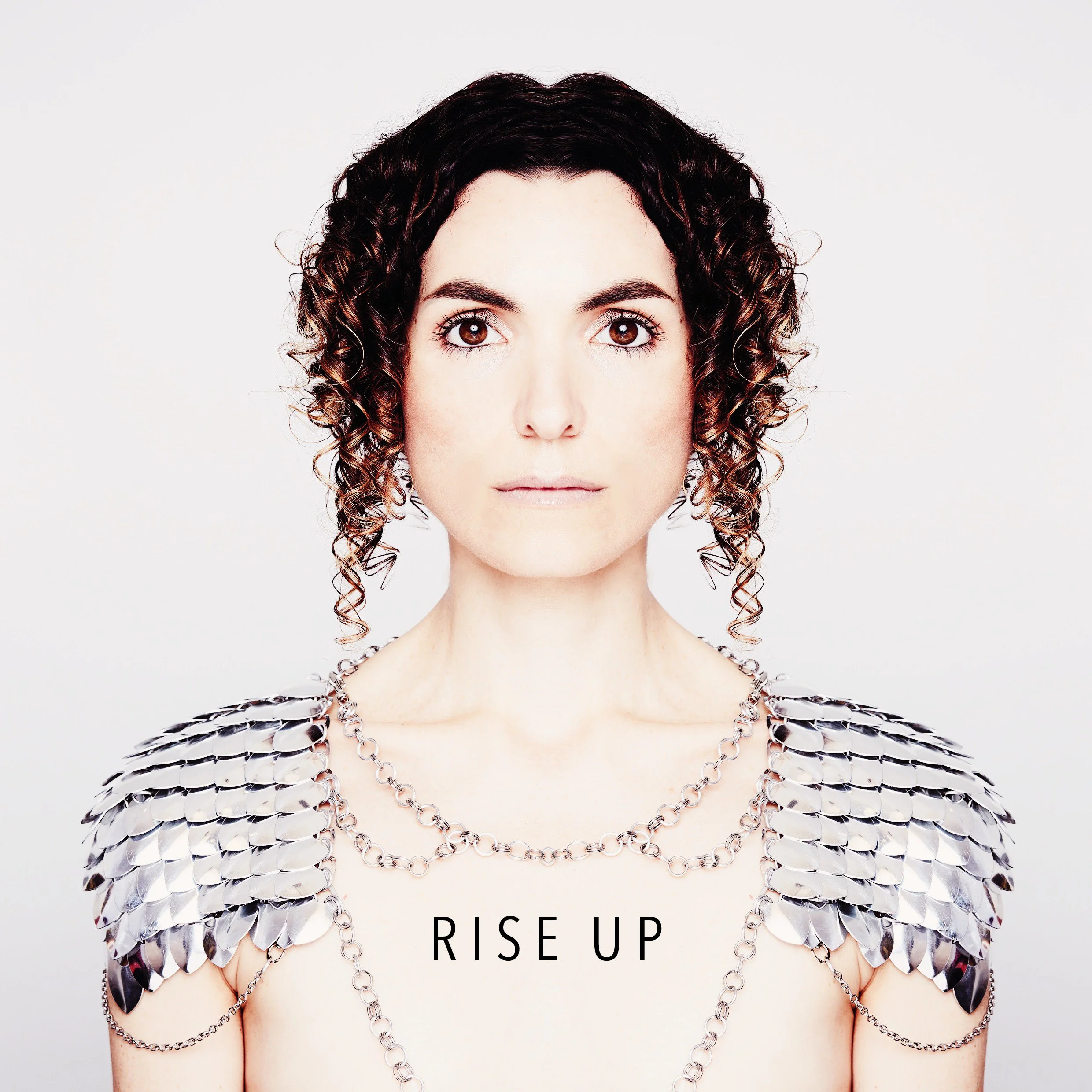 Close-up of Jessica O'Donoghue with dark, curly hair and brown eyes, wearing layered silver chains. The background is plain white with the text "RISE UP" at the bottom.