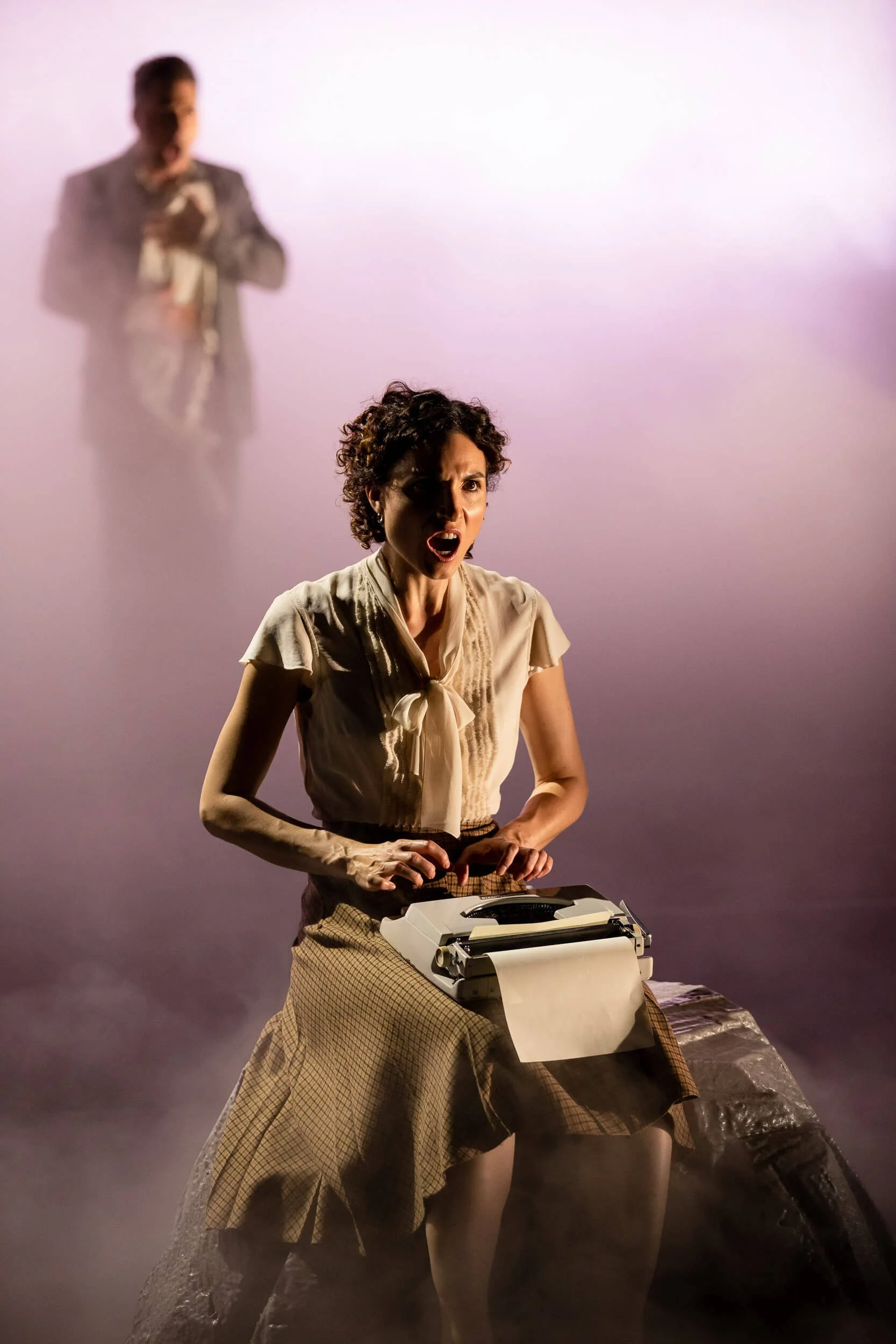 Jessica O'Donoghue with short curly hair passionately singing or shouting while standing in front of a vintage typewriter.