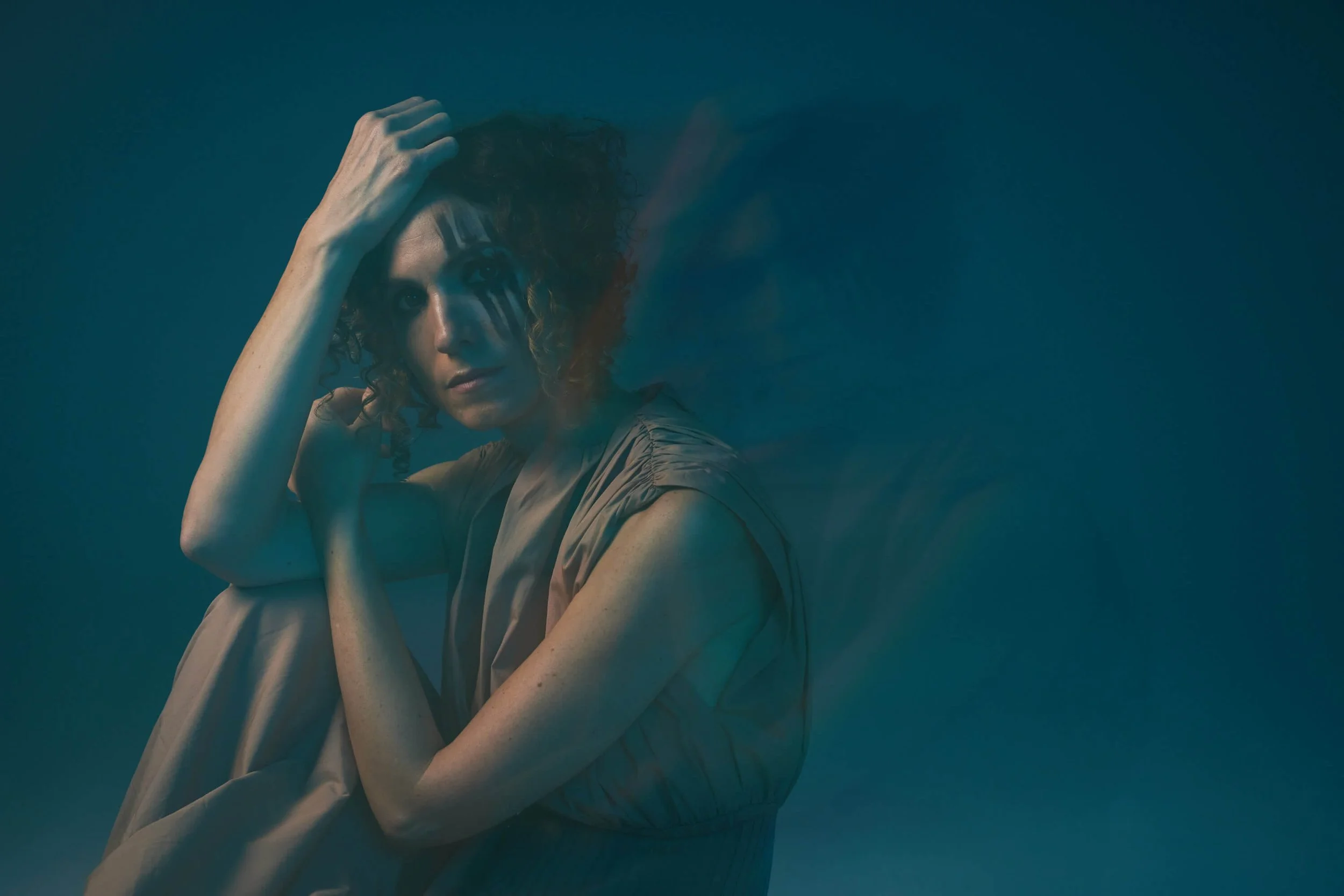Jessica O'Donoghue with curly hair poses with her hand on her head against a dark teal background.