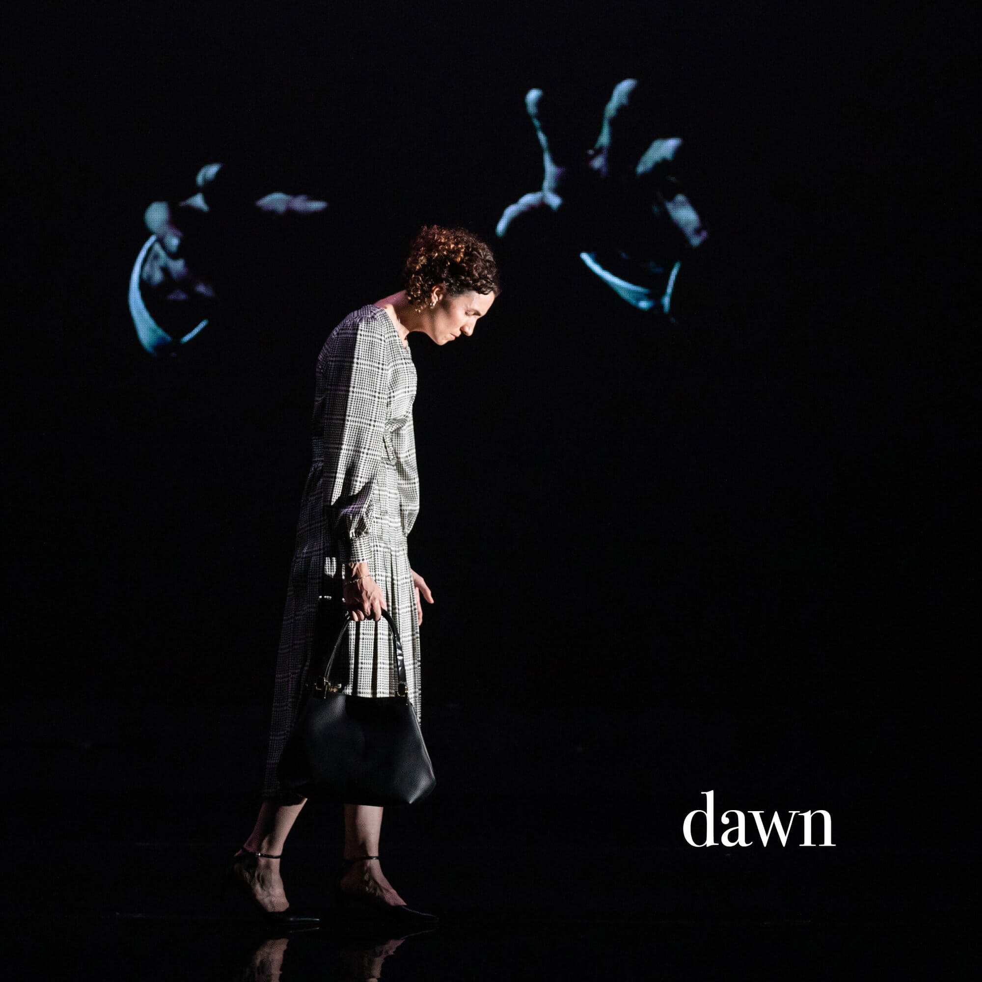 Jessica O'Donoghue in a checkered coat walking in the dark with a large digital display behind her showing a giant spider and the words 'dawn' and 'new day'