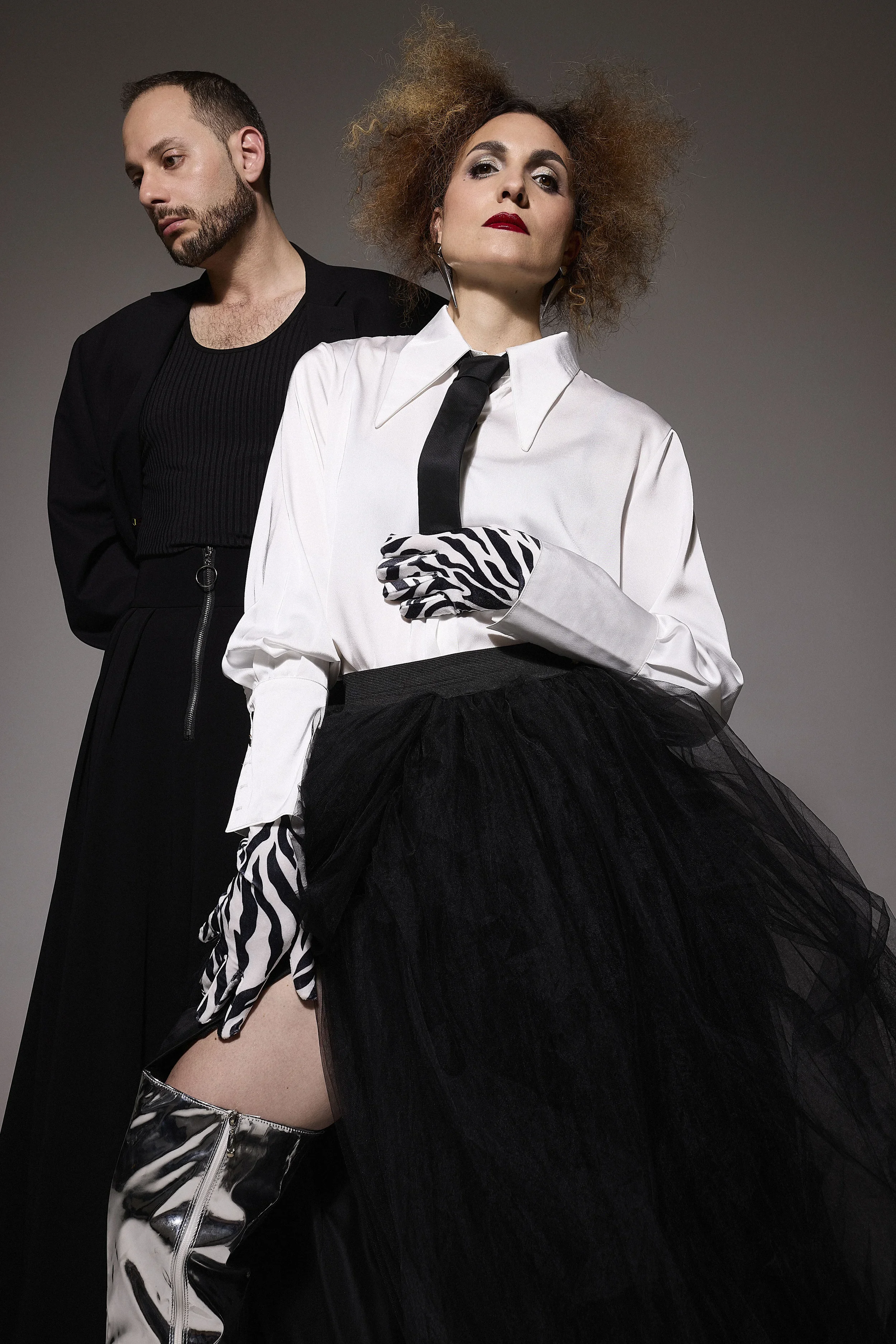 Jessica and Jack posing against a plain background, one wearing a black jacket and the other in a white shirt with a black tie and a black tulle skirt. 