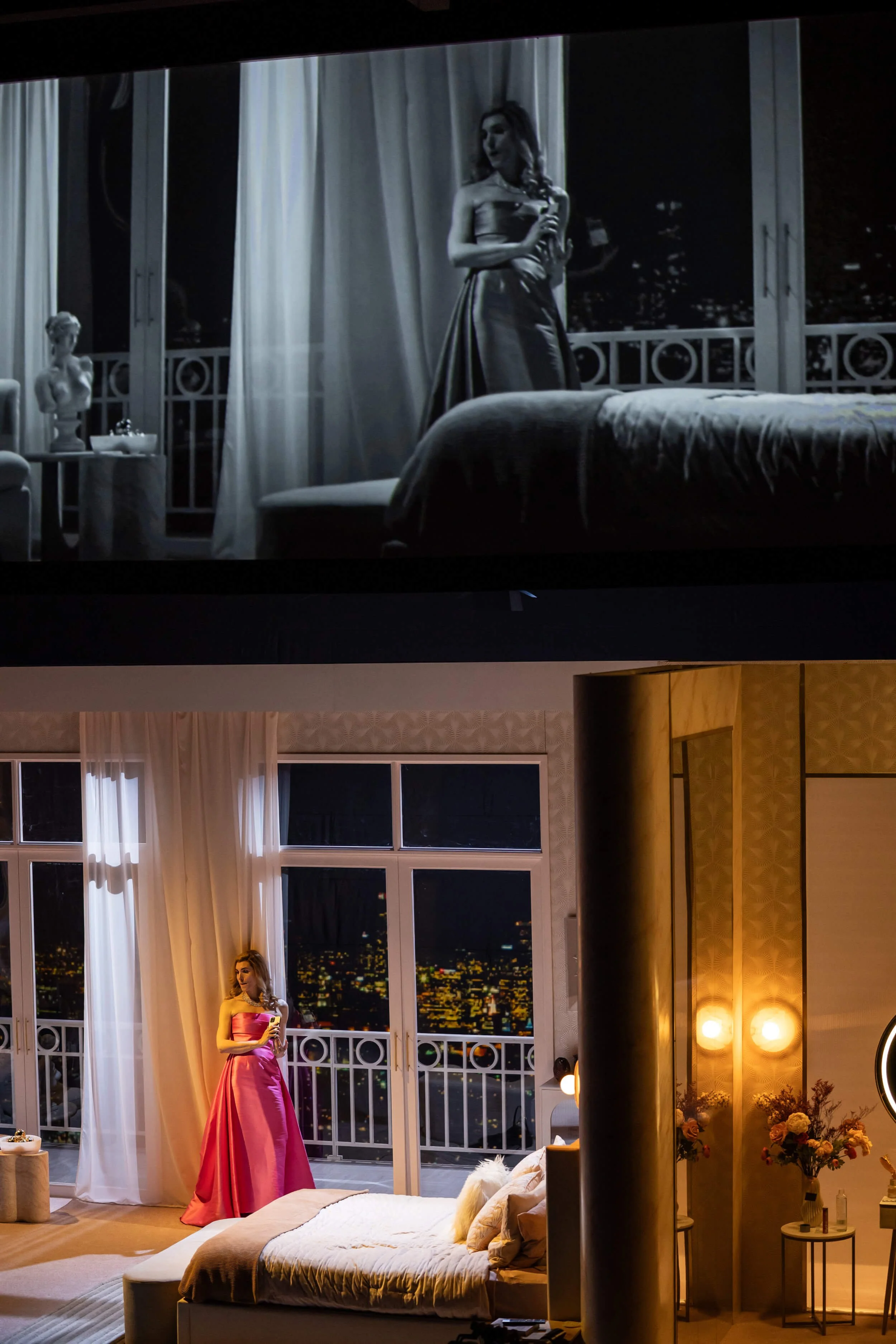 Jessica O'Donoghue in a pink gown stands in a stylish, well-lit apartment with large windows at night, city lights visible outside. 