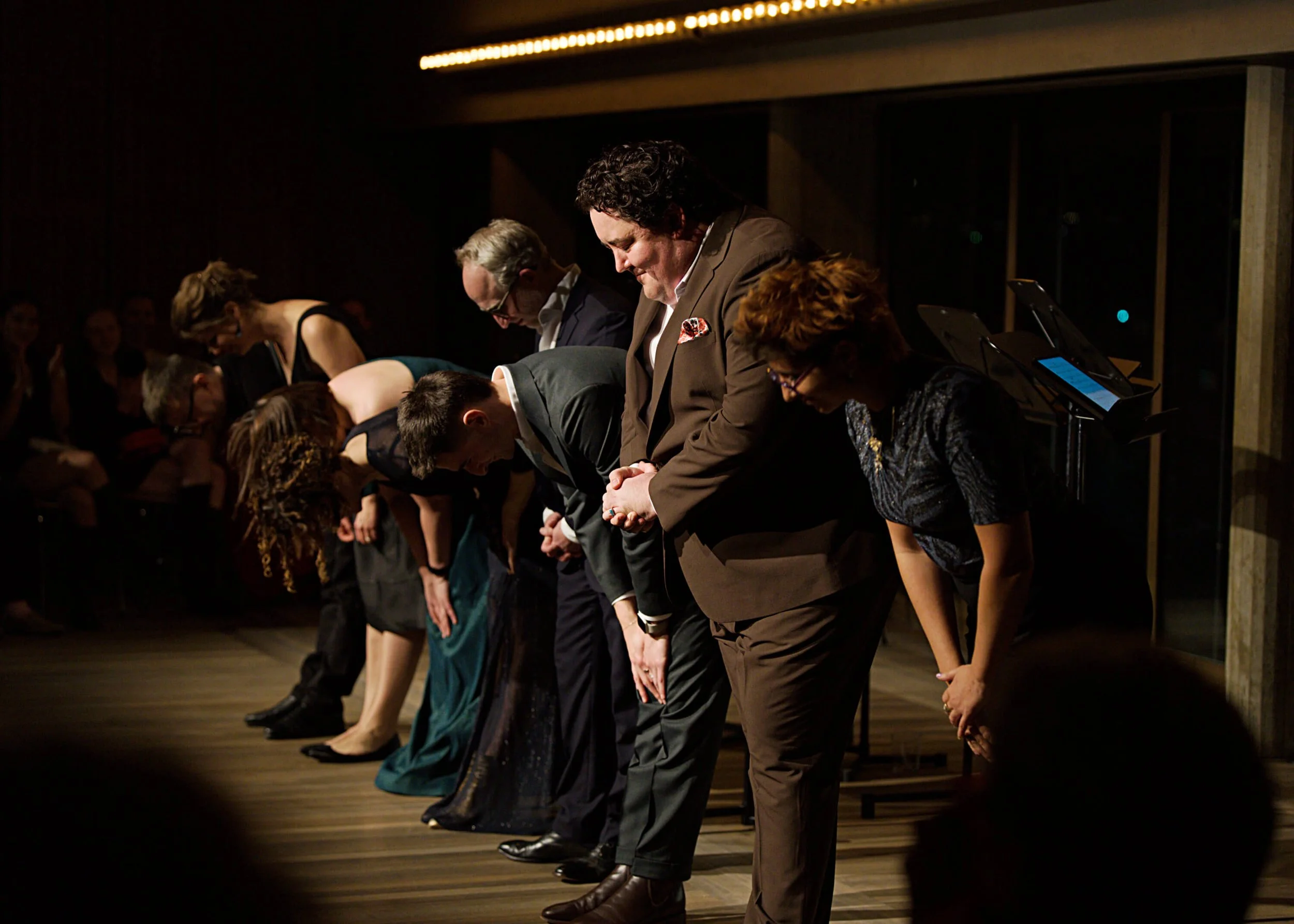 A group of people dressed in formal attire bowing on stage after a performance.