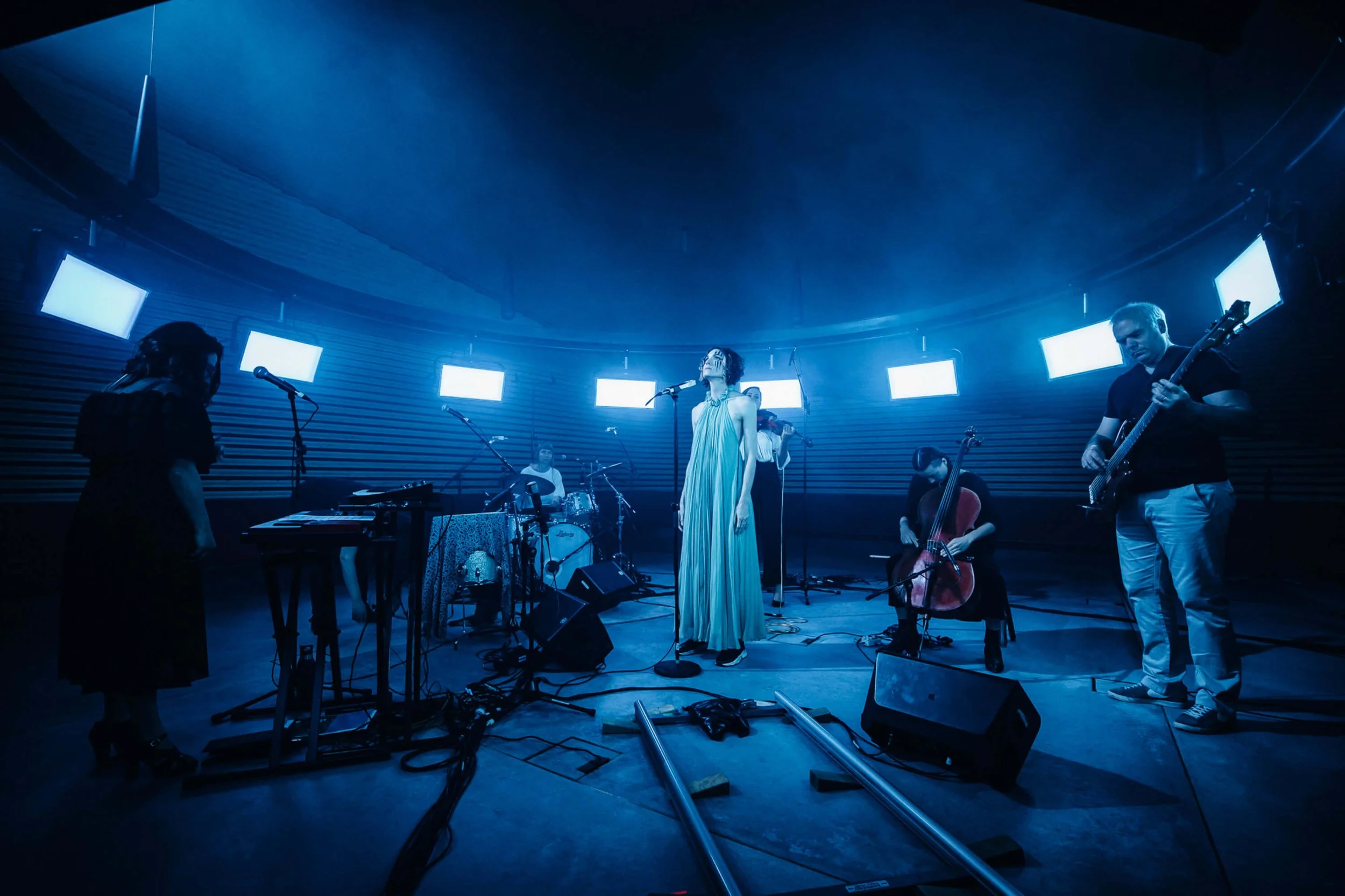 Jessica O'Donoghue in a flowing dress performing with a band on a dimly lit stage with blue lighting and multiple monitors.