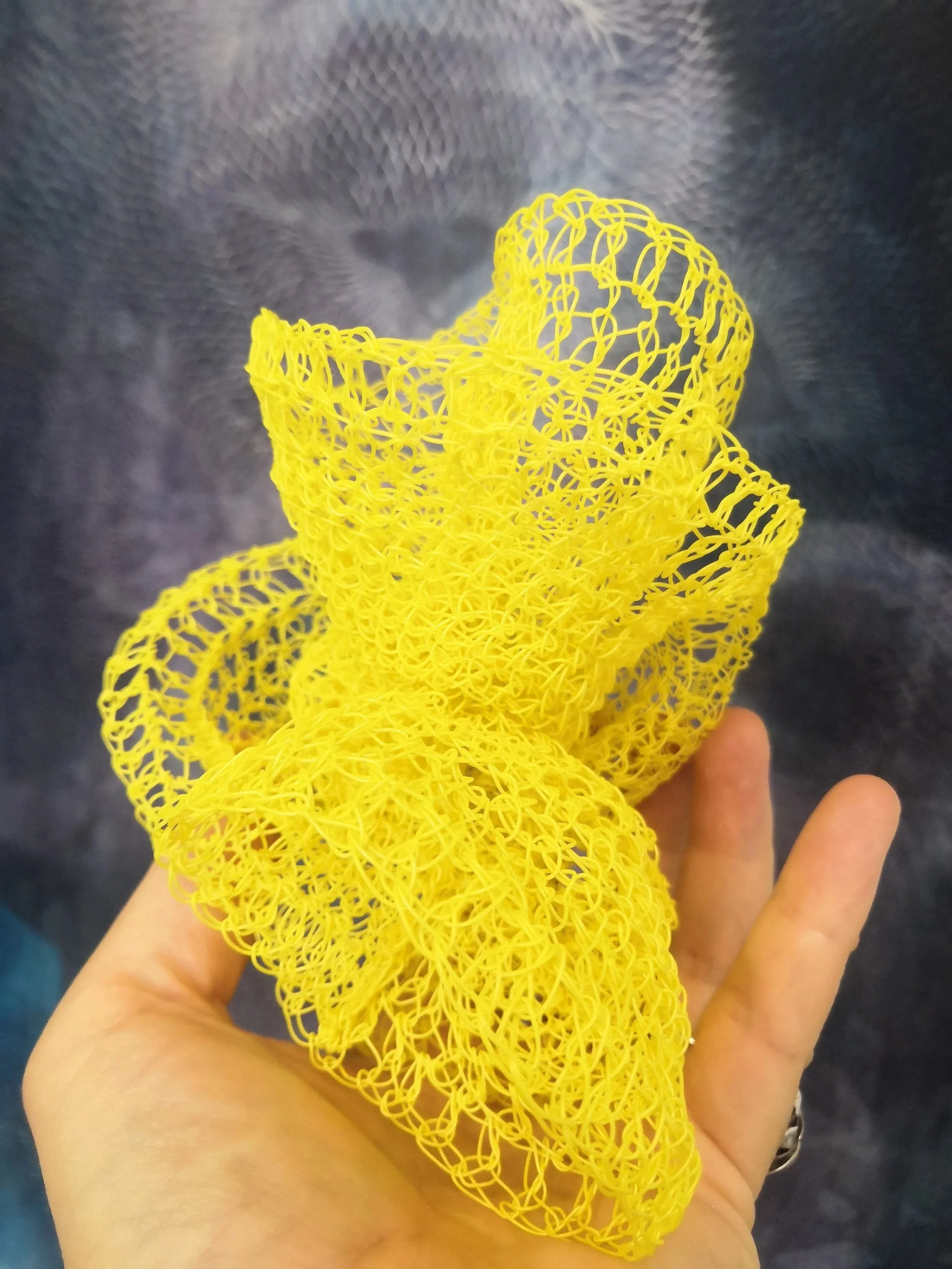 A person holding a yellow plastic scrubber with a mesh-like structure in front of a dark textured background.