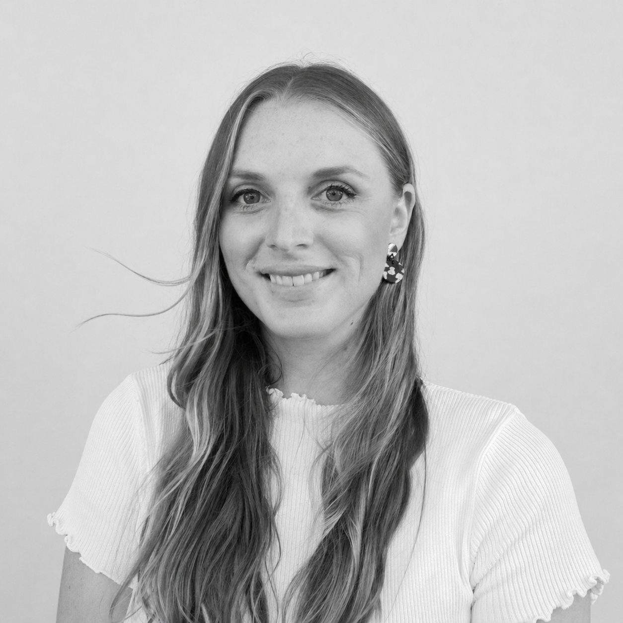 Black and white portrait of a smiling young woman with long wavy hair, wearing a light-colored top and patterned earrings.
