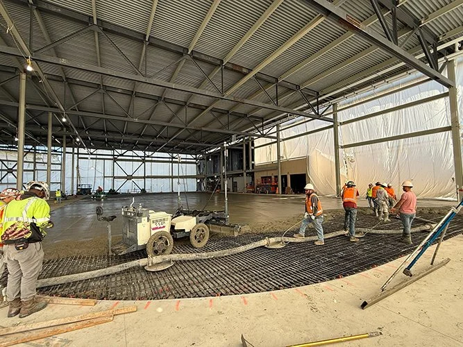 jscreed pouring and smoothing concrete floor inside a large industrial building or warehouse.