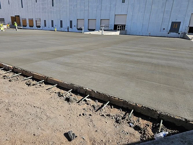 Newly poured concrete by jscreed, next to a building under construction with  and construction materials in the background.