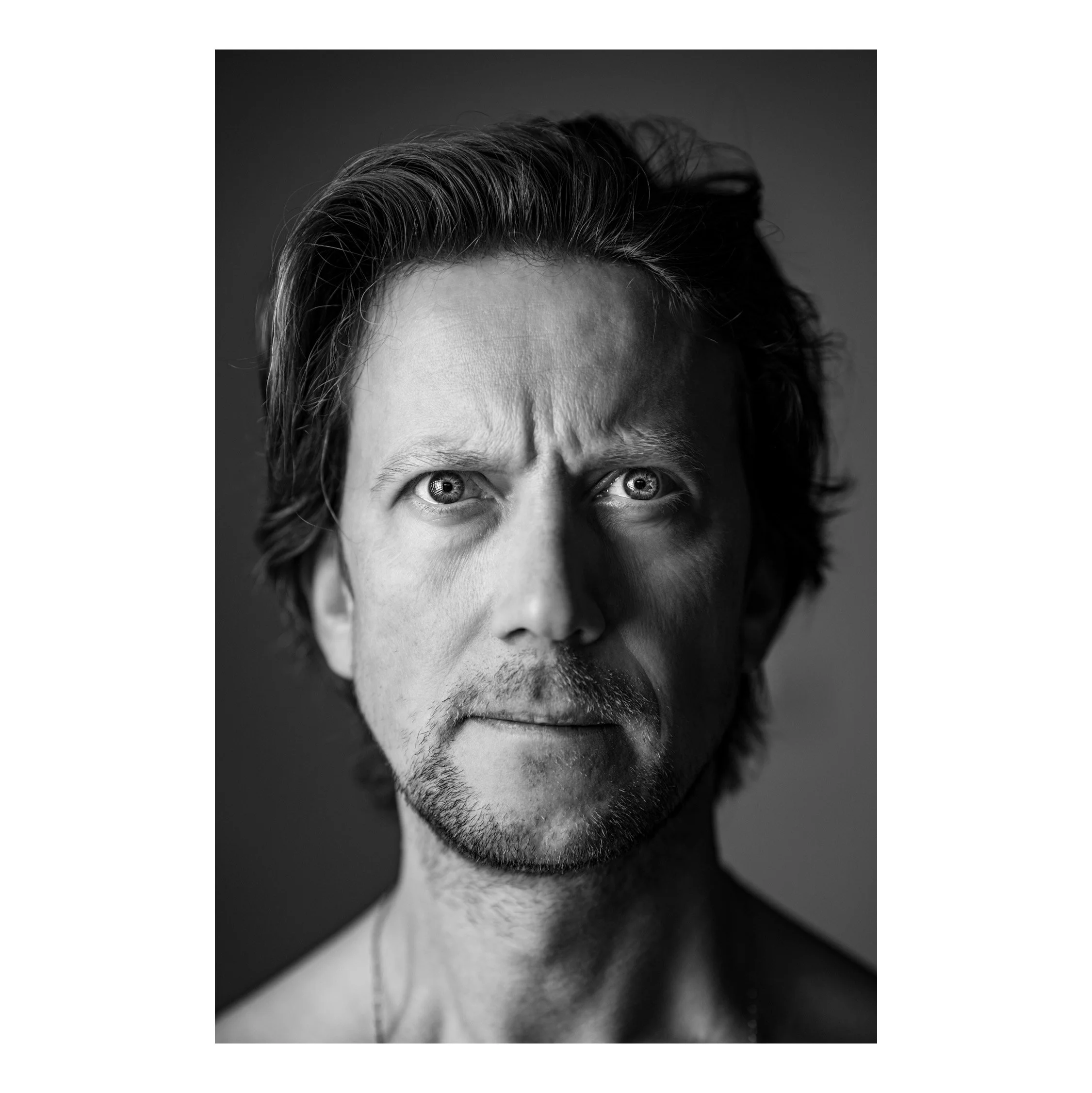 Shooting Portrait “blckndwht”-Style Schwarz-weiß Porträt eines Mannes mit dunklen, zerzausten Haaren, sichtbare Stirnfalten und intensiven Blick in die Kamera.
