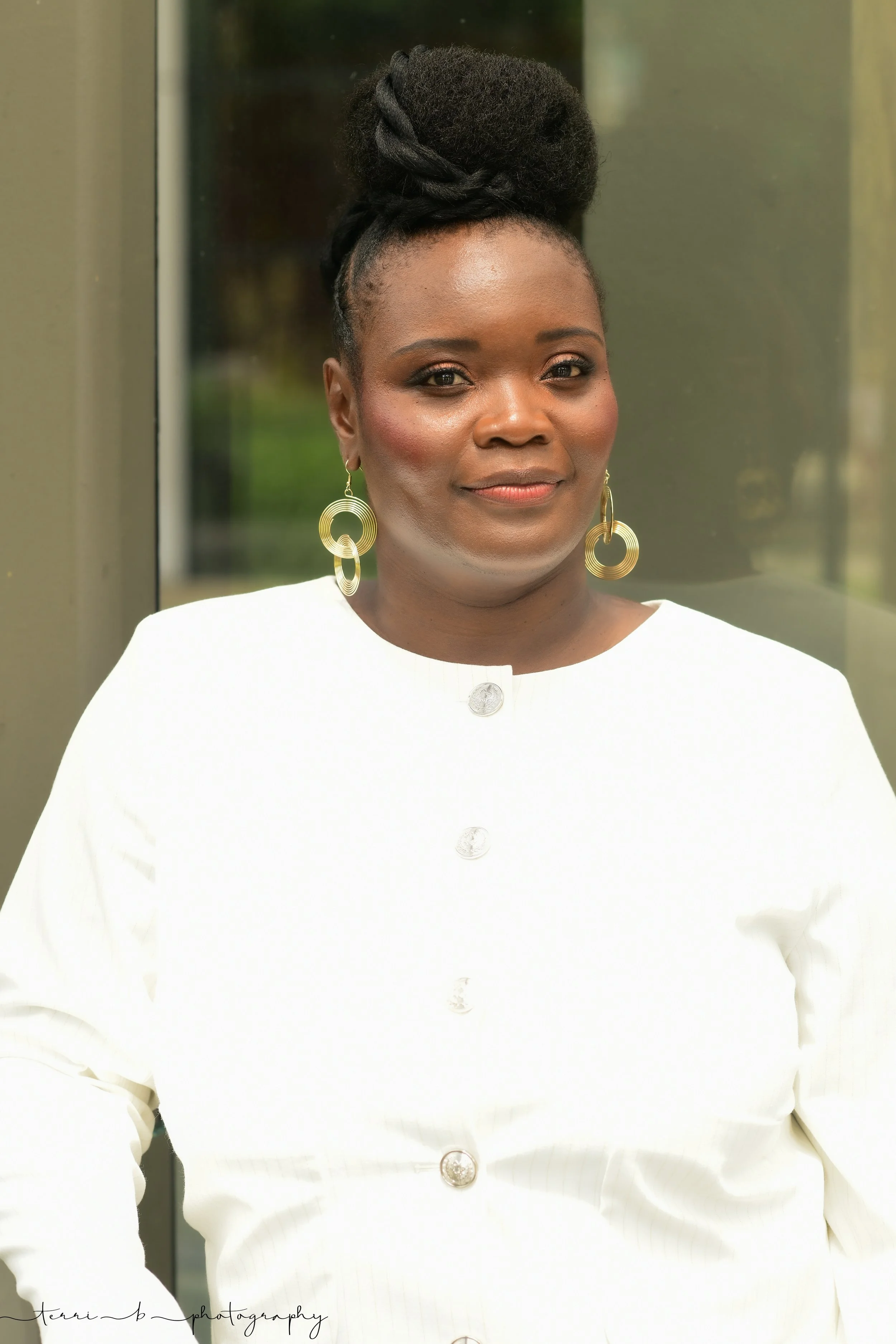 Strong woman building Journey to Brave wearing a natural updo,  a white jacket with gold stripes and gold hoop earrings.