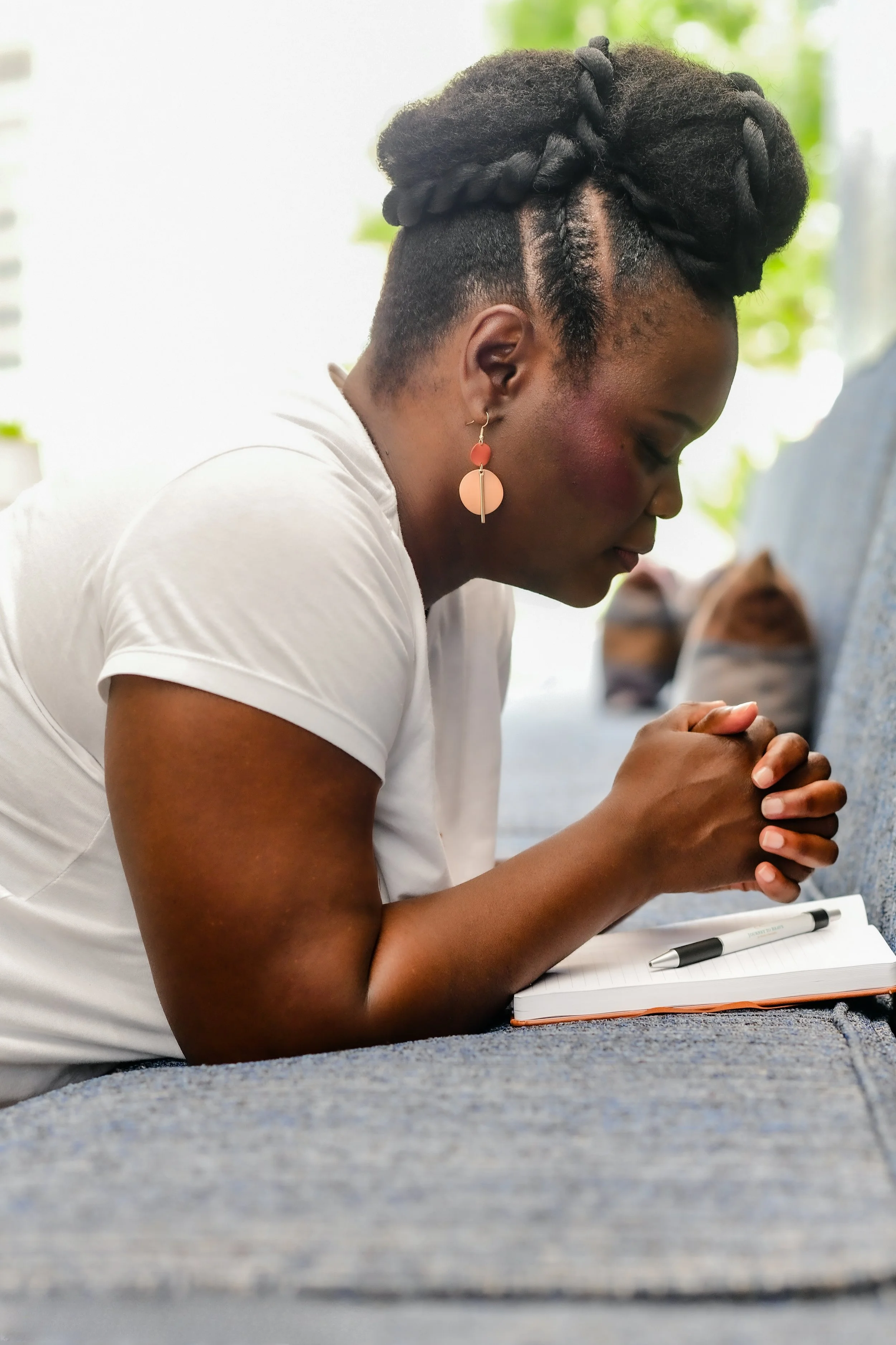 Black woman with a natural updo with her eyes closed and praying.