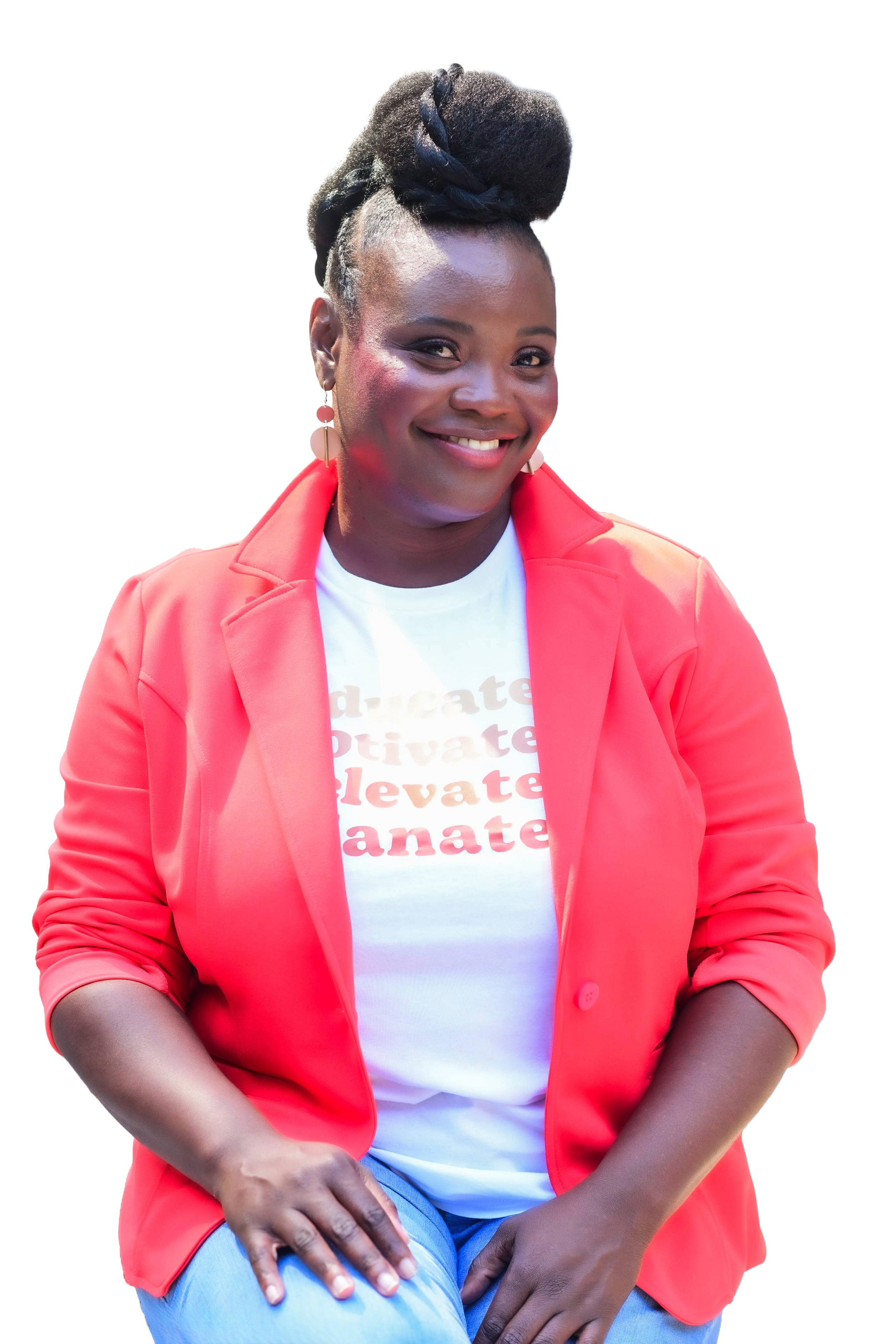 A woman smiling, wearing a white t-shirt with red text, a bright coral blazer, and light blue jeans. She has dark hair styled in an updo wearing earrings.