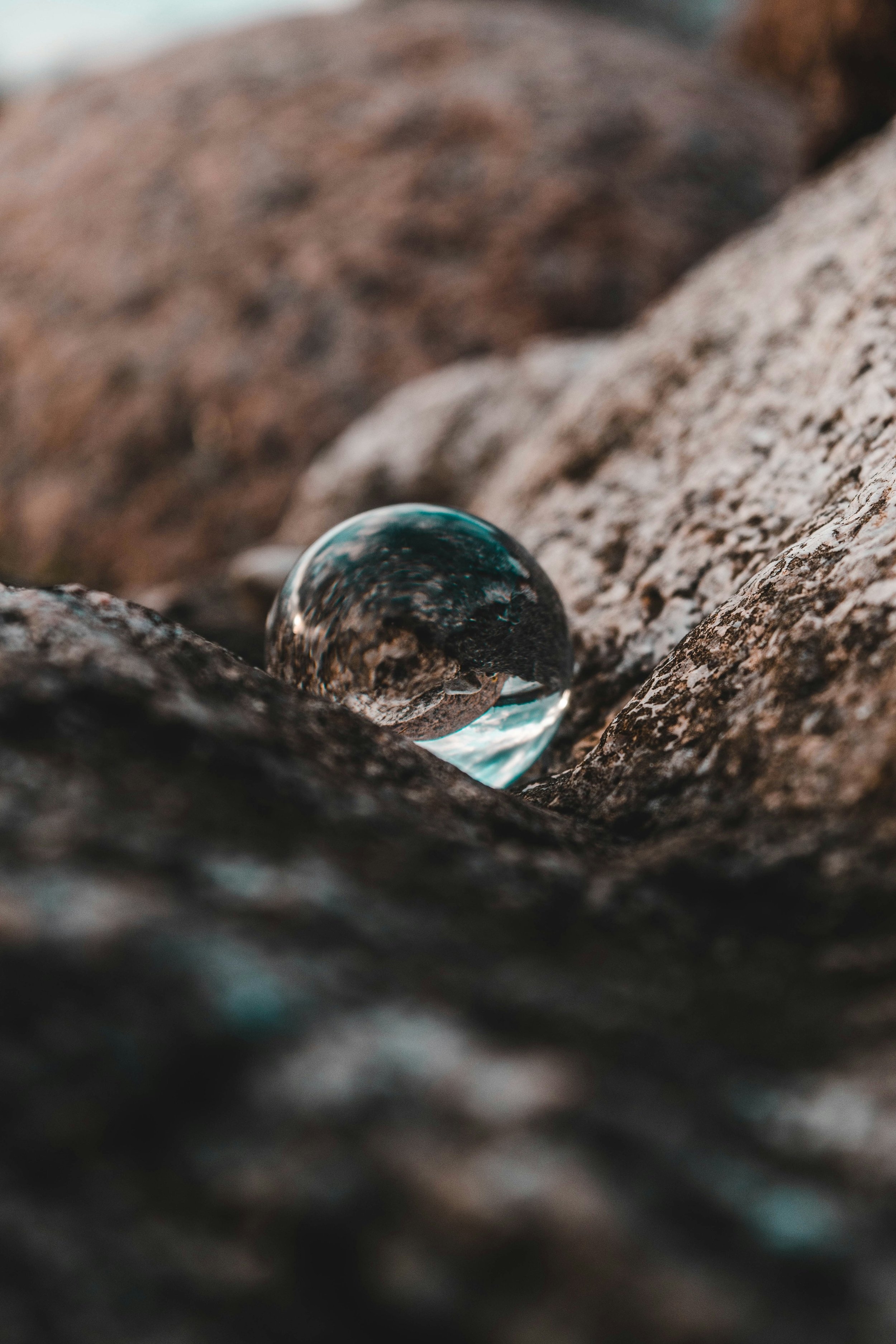 Close-up of a polished, glass marble resting on a textured rock surface with a blurred rock background.